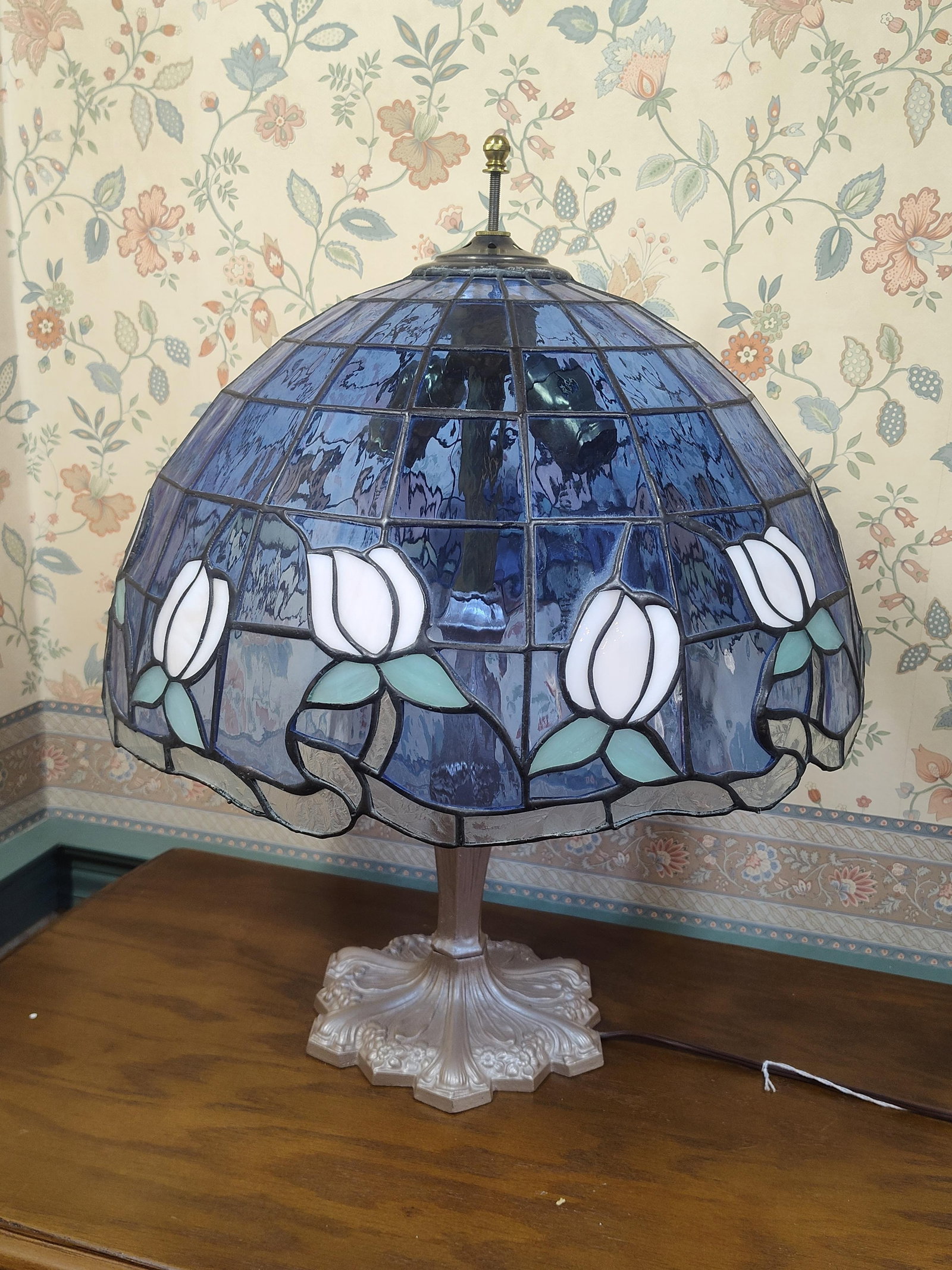 Tiffany Style Leaded Glass Tulip Motif Table Lamp: This Tiffany-style table lamp features a domed leaded glass shade and a cast metal base. The shade is constructed from blue slag glass panels with a textured, rippled surface, decorated with a repeati