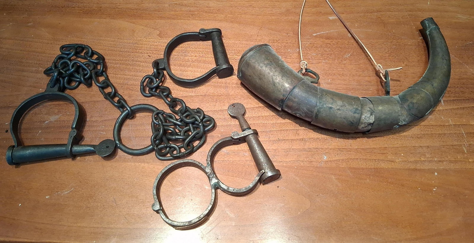 19th C. Style Iron Restraints & Balkan Signal Horn: This group comprises two sets of iron restraints and one decorative signal horn. The first set of restraints consists of heavy iron leg shackles connected by a hand-forged style chain to a large