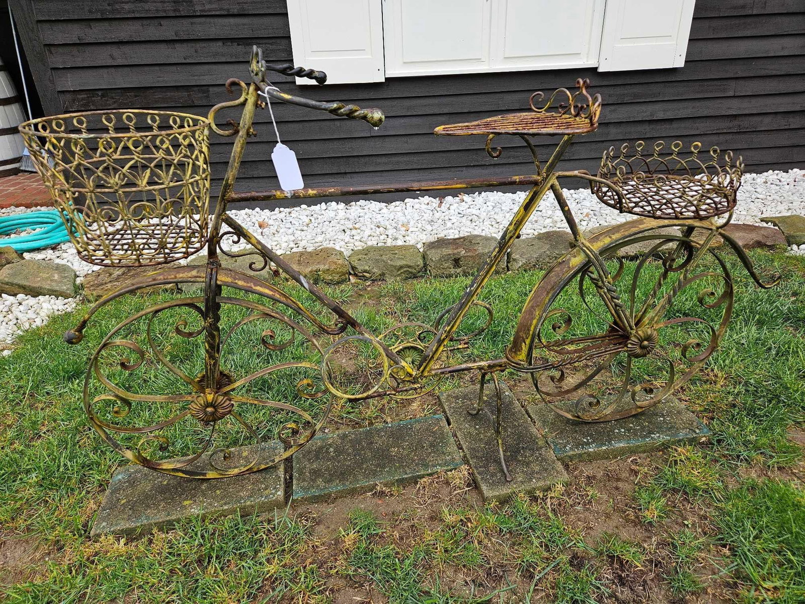 Wrought Iron Bicycle Garden Planter: A large-scale decorative garden planter constructed from wrought iron and steel, fashioned in the style of a vintage bicycle. The piece features intricate scrollwork detailing forming the wheel