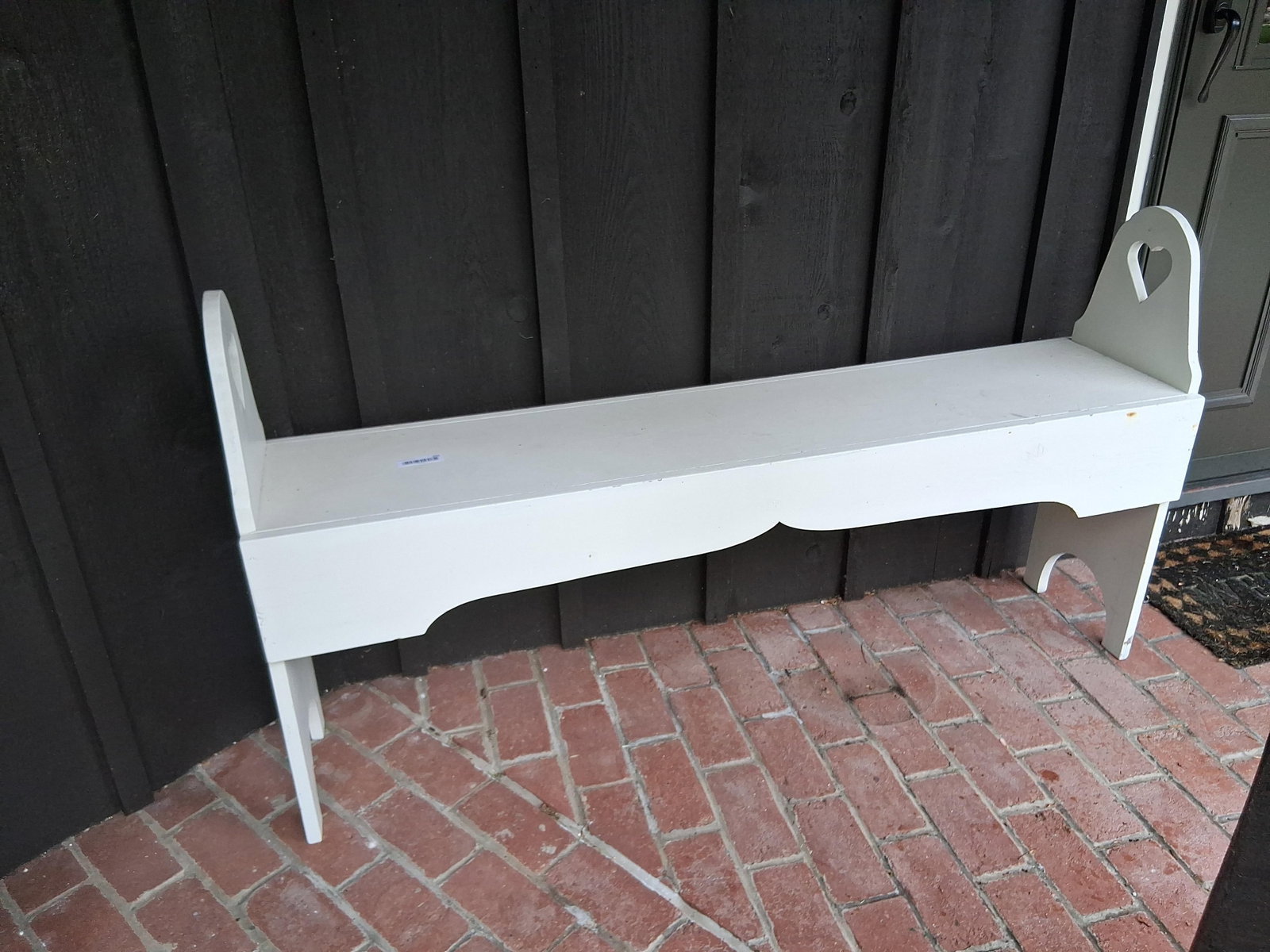 Primitive White Painted Wood Bench w/ Hearts: 58 inches long. This primitive style wooden bench is constructed from solid wood planks and finished in white paint. The piece features high, integrated side panels that serve as both the legs and