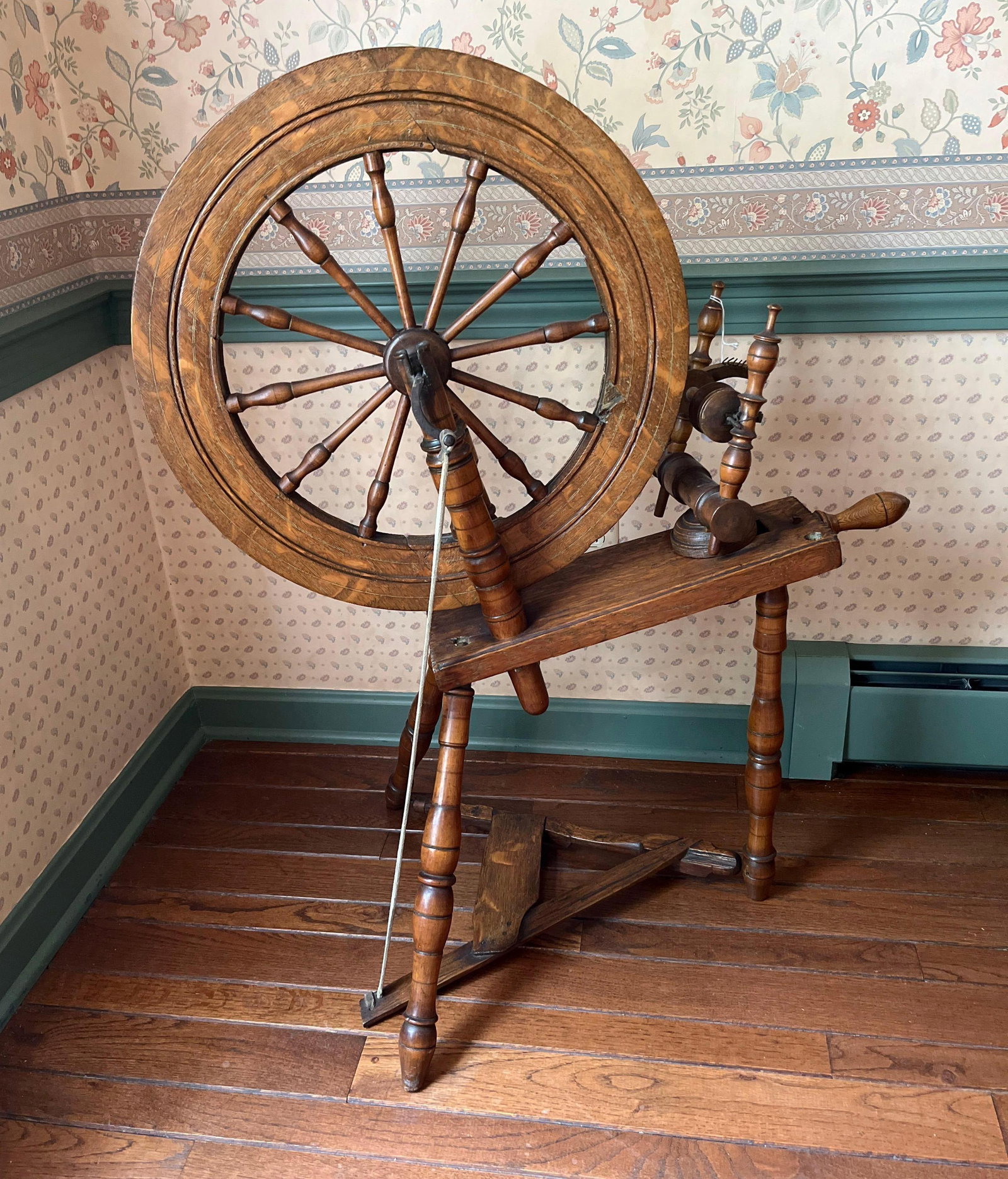Mid-19th C. Style Wooden Saxony Spinning Wheel: A traditional Saxony-style spinning wheel crafted from a hardwood, likely oak, featuring a prominent natural grain. The assembly is supported by three lathe-turned legs arranged in a tripod