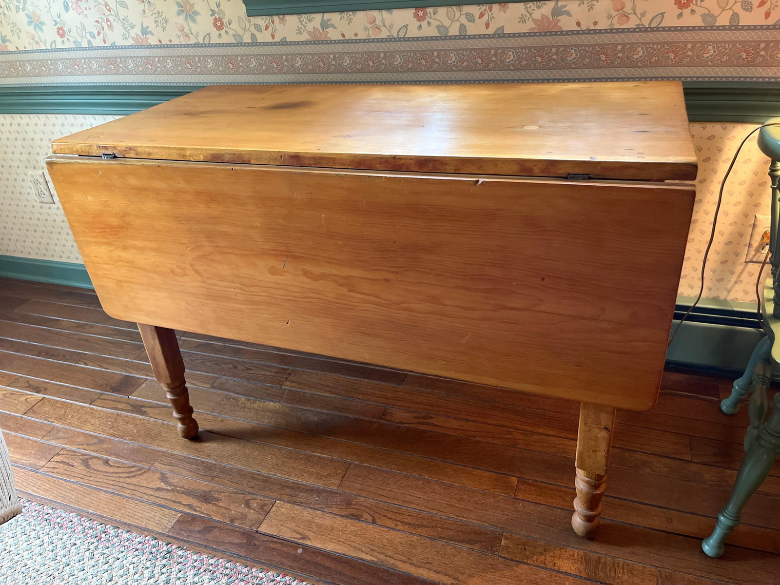 American Country Solid Wood Drop Leaf Dining Table: This American Country style drop leaf dining or work table is constructed from solid wood, featuring a grain and honey-toned finish characteristic of maple or pine. The design consists of a