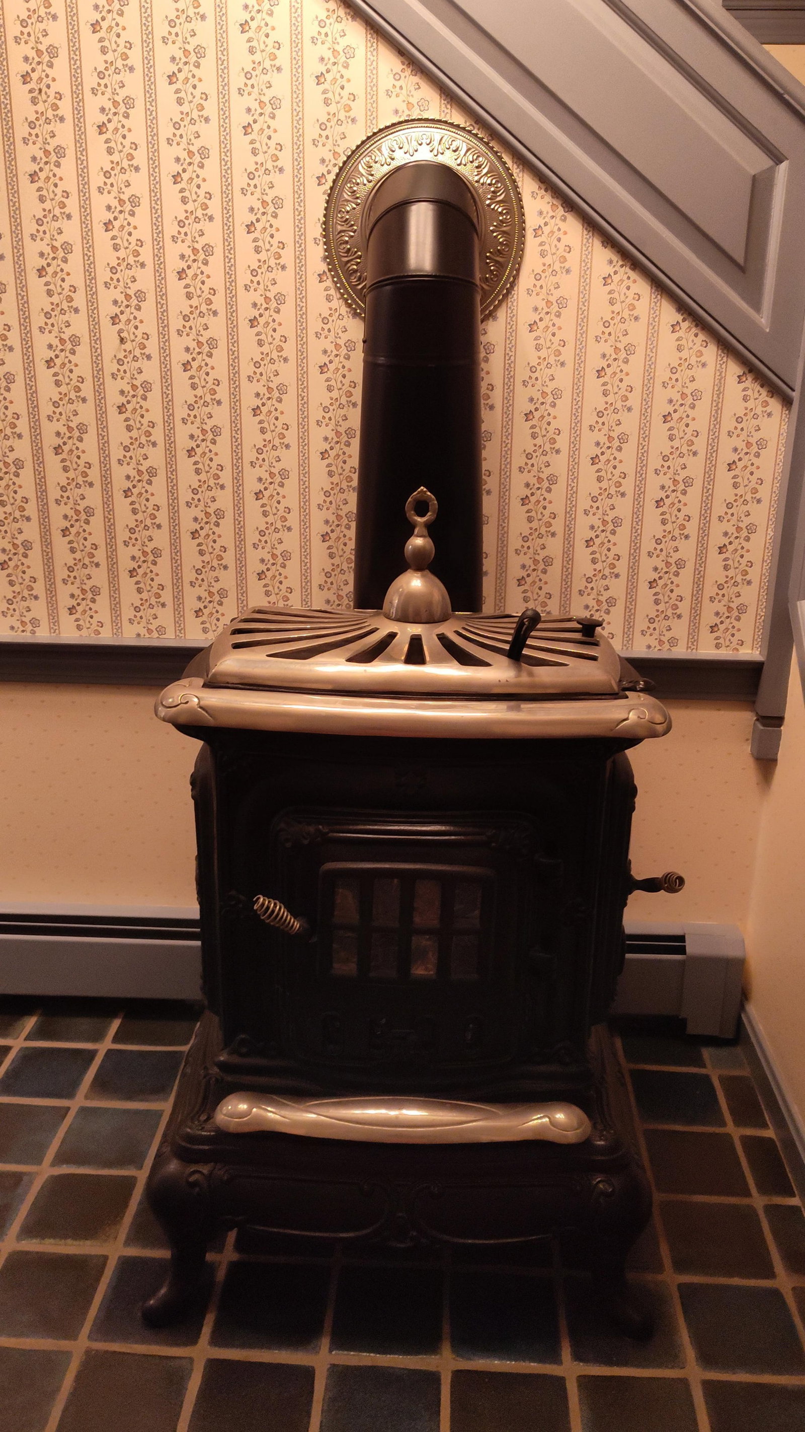 Victorian Wood Burning Parlor Stove: A wood-burning parlor stove in the Victorian style, constructed from cast iron with decorative nickel-plated accents. The unit features a hinged top with a sunburst-patterned grate and a central