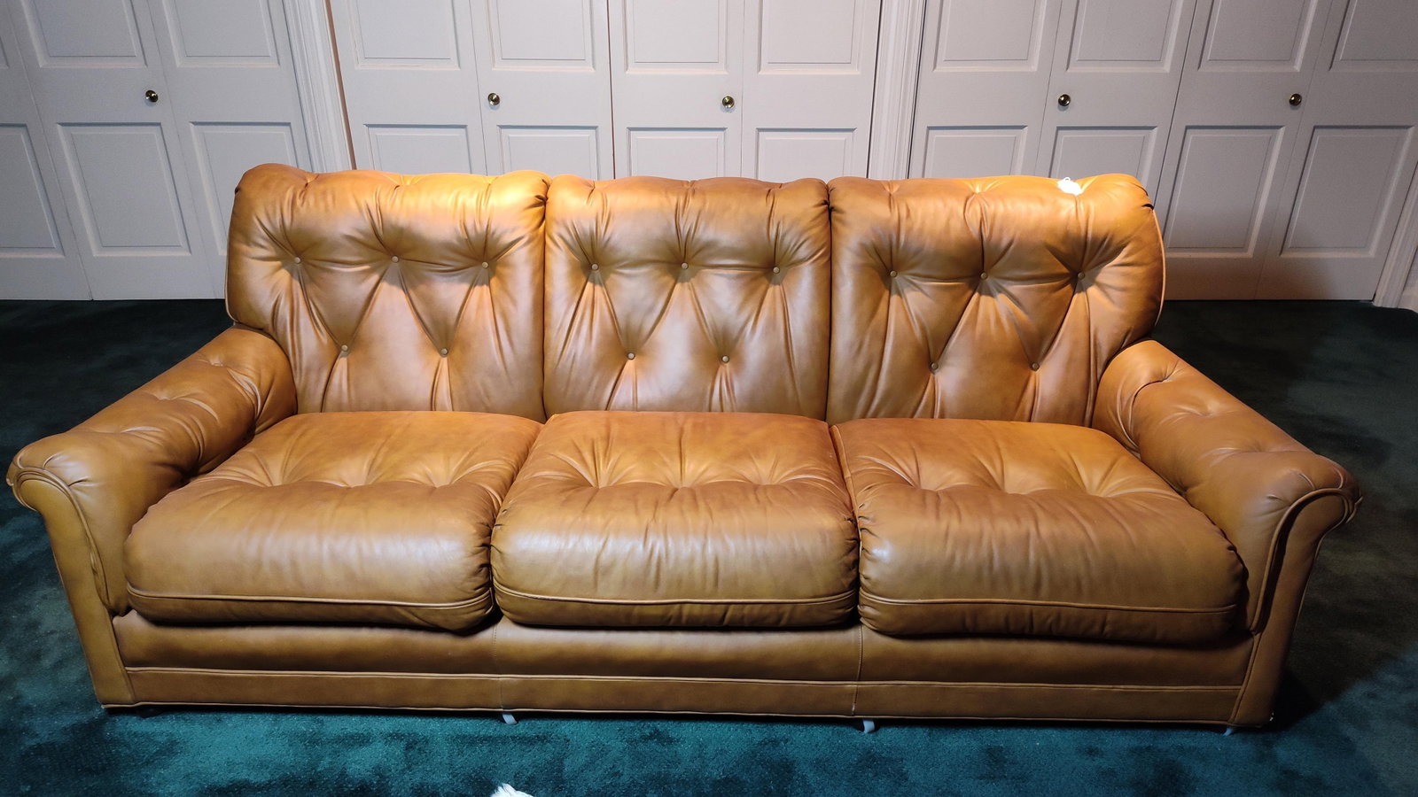 Vtg Post-Modern Biscuit Tufted Leather 3-Seat Sofa: 84 inches. This three-seat sofa features a fully upholstered frame with a low profile and rolled arms. The design is characterized by deep biscuit tufting across the backrest, interior arms, and the