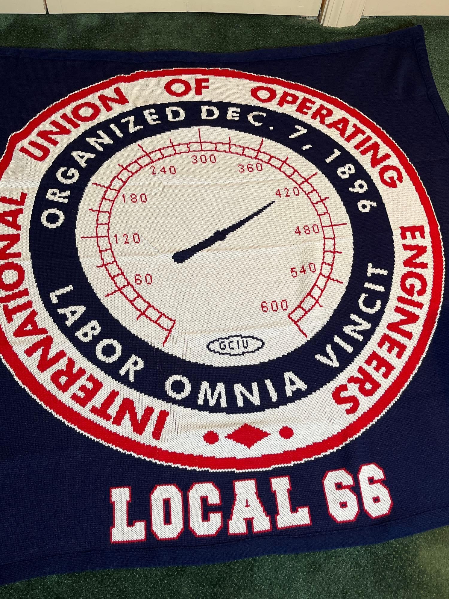 Union of Operating Engineers Throw: A jacquard knit commemorative textile for the International Union of Operating Engineers (IUOE) Local 66. The piece is constructed on a navy blue ground with a large central seal designed in the form 