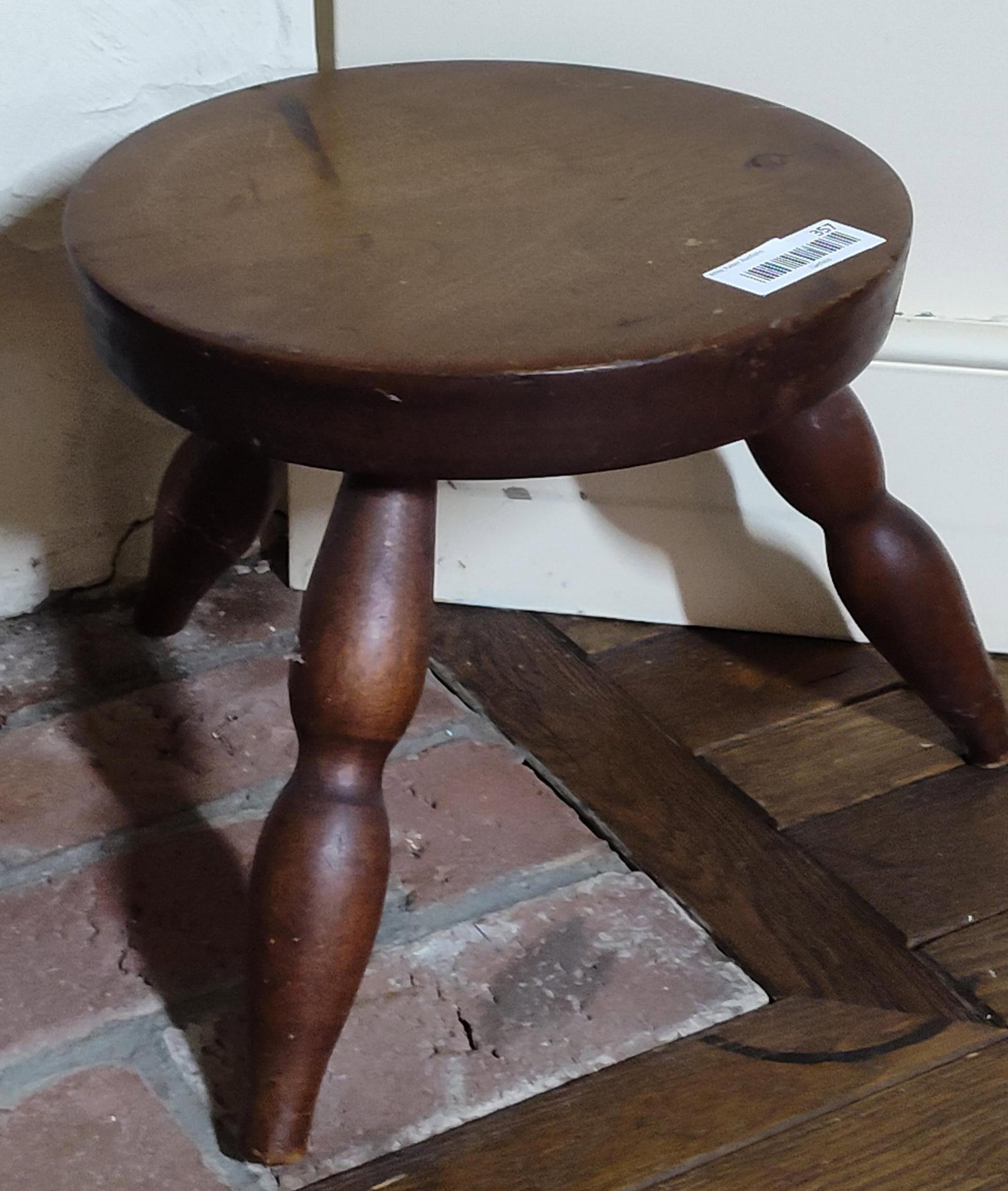 Vintage Three Legged Wooden Milking Stool: A vintage three legged wooden stool, commonly referred to as a milking or cricket stool. The item features a thick, circular seat supported by three splayed, turned legs in a bulbous baluster form. Th
