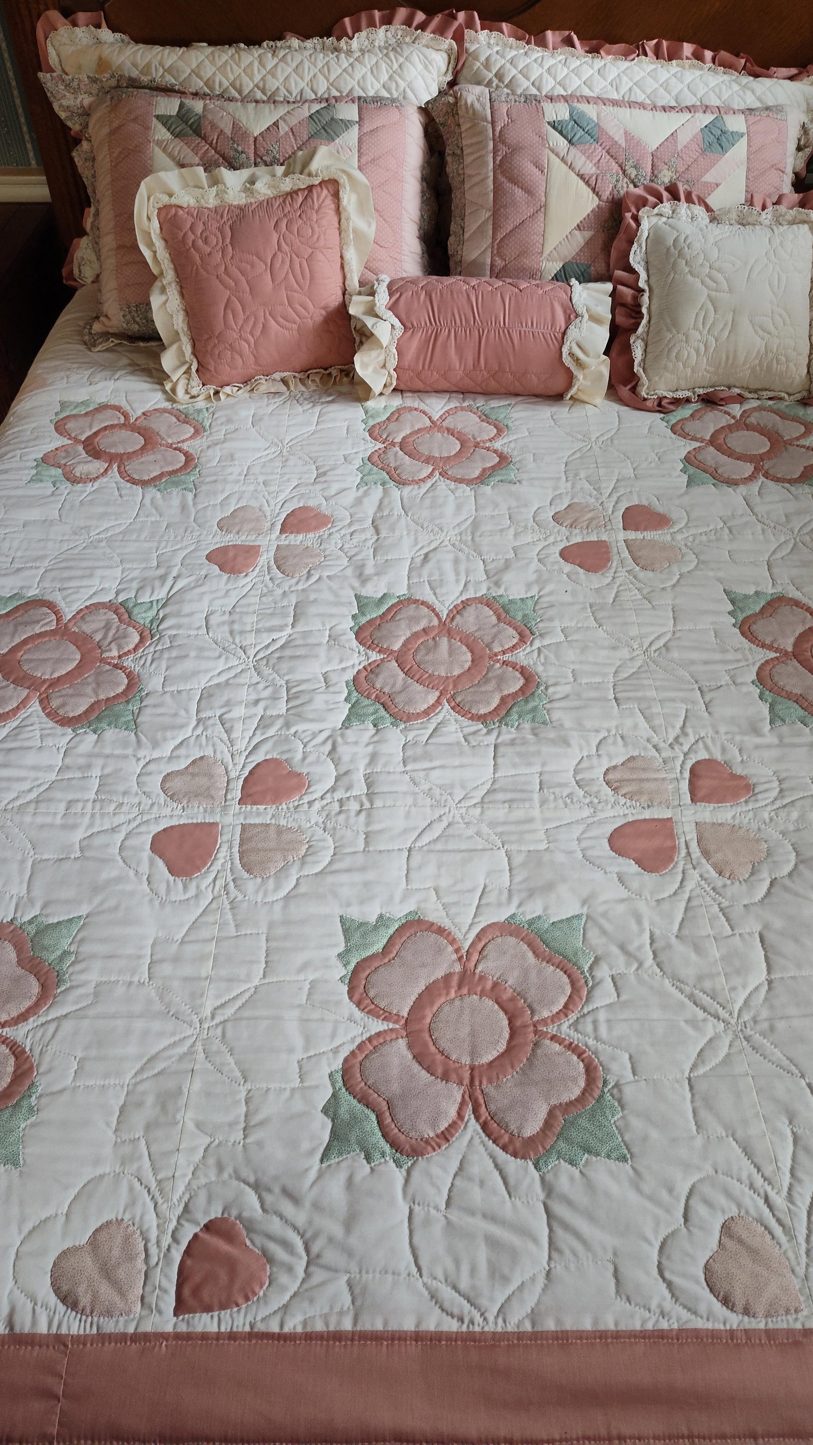Floral Appliqu? & Patchwork Quilted Bedding Set: A set of quilted bedding featuring a traditional country cottage aesthetic. The collection includes a large coverlet with scalloped edges, large patchwork shams, square decorative pillows, a cylindric