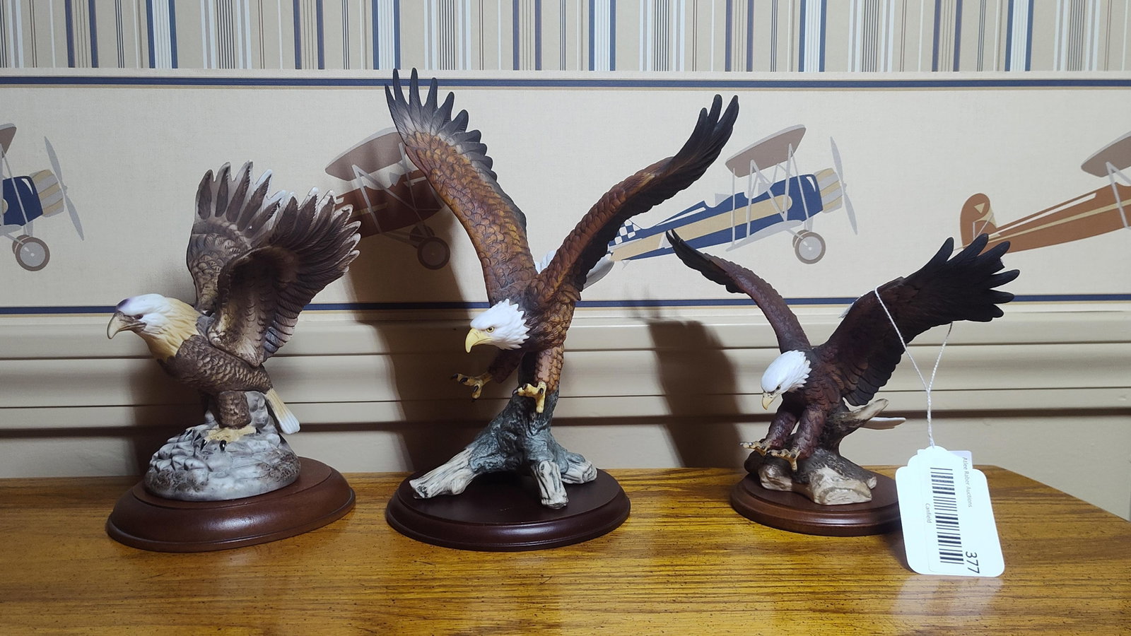 Trio of Hand-Painted Porc. Bald Eagle Figurines: This collection consists of three hand-painted bisque porcelain bald eagle figurines, each mounted on a finished circular wooden base. The central figurine is definitively identified by a gold-tone