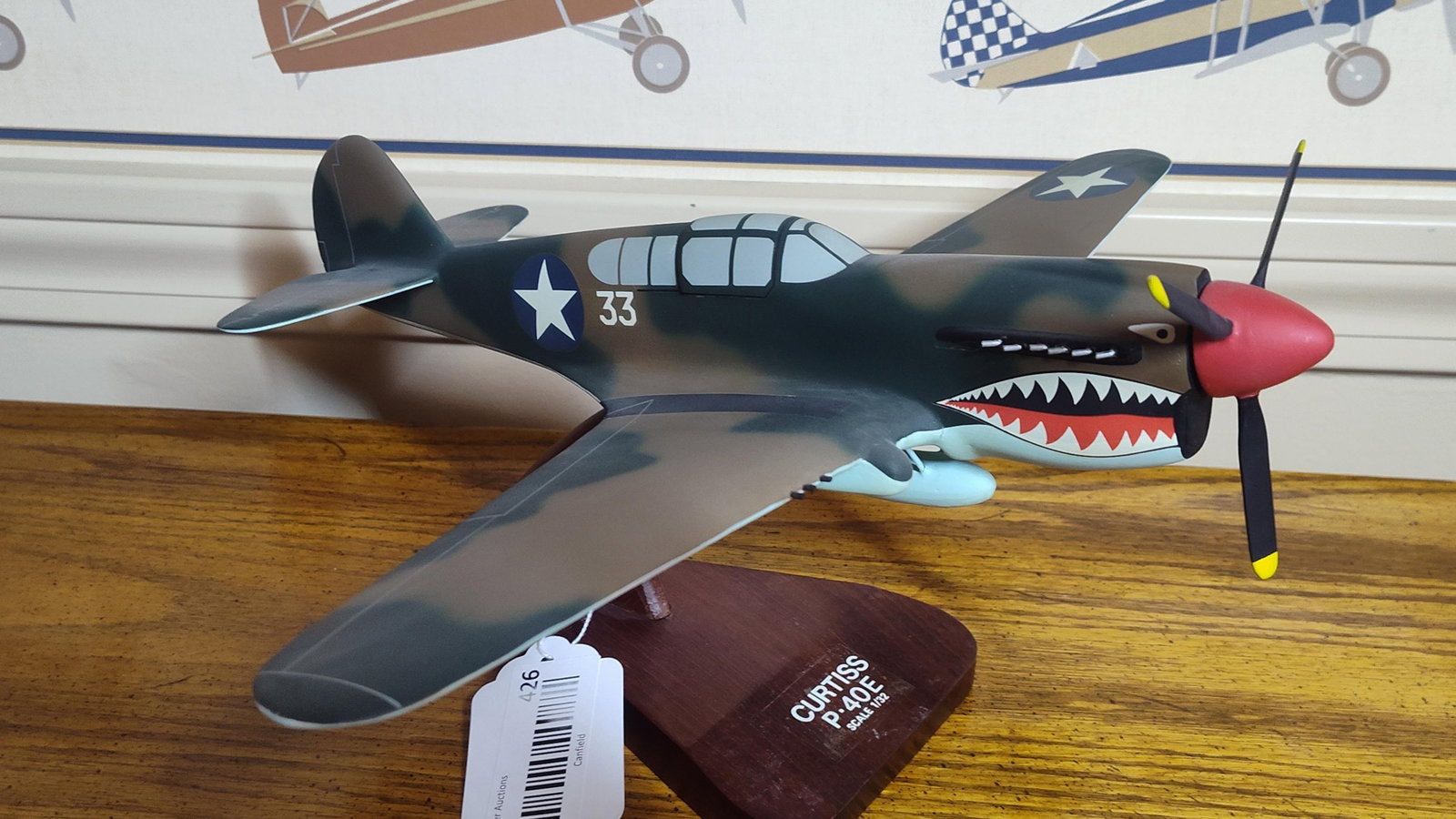 Curtiss P-40E Warhawk Hand-Carved Wood Desk Model: This is a hand-carved wooden desktop display model of a Curtiss P-40E Warhawk fighter aircraft, constructed in 1/32 scale. The model is finished with a matte camouflage paint scheme consisting of