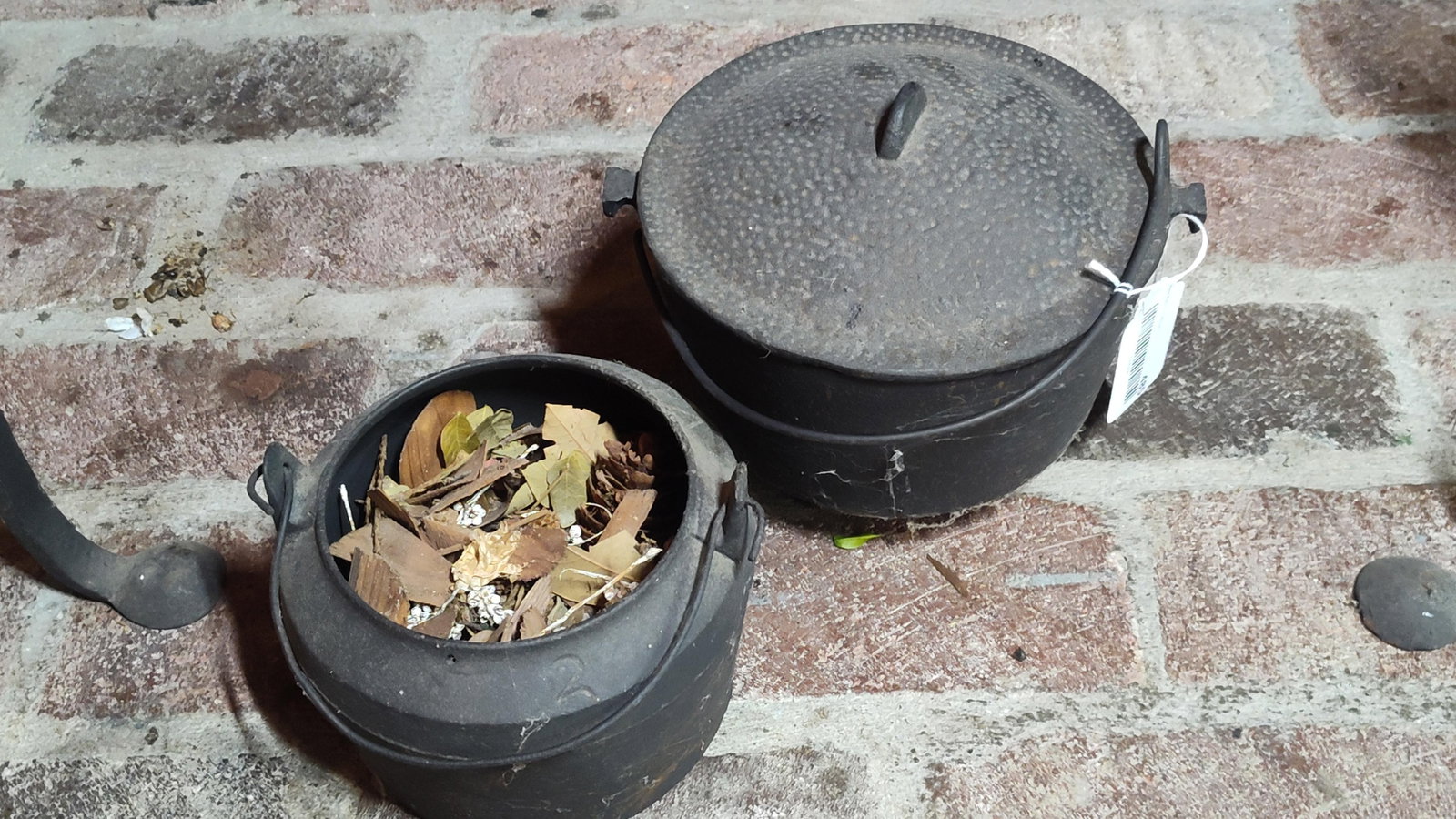 Two Vintage Cast Iron Cooking Pots: This lot consists of two vintage cast iron cooking pots, commonly referred to as cauldrons or kettles. Both items are constructed of heavy cast iron and feature integrated side lugs with attached