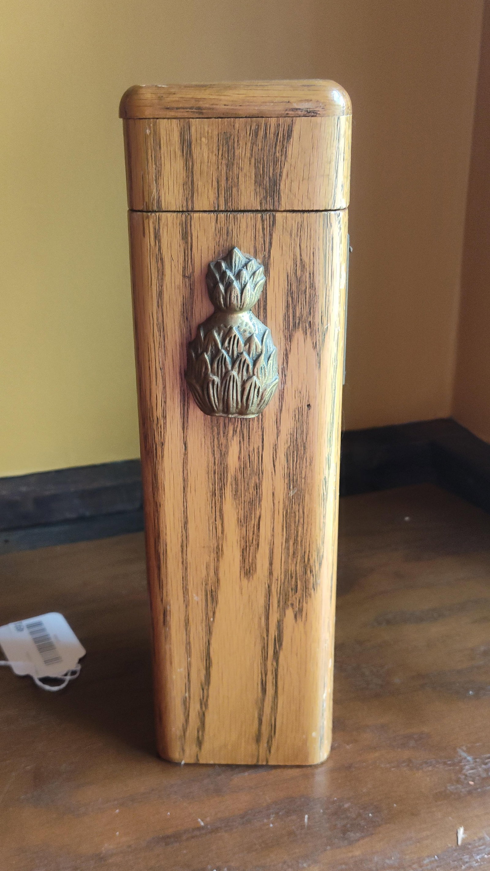 Vintage Wood Storage Box with Pineapple Applique: A vintage tall rectangular wooden storage box featuring a cast metal pineapple applique on the front face. The box is constructed from wood with a vertical grain and a light honey-toned finish,