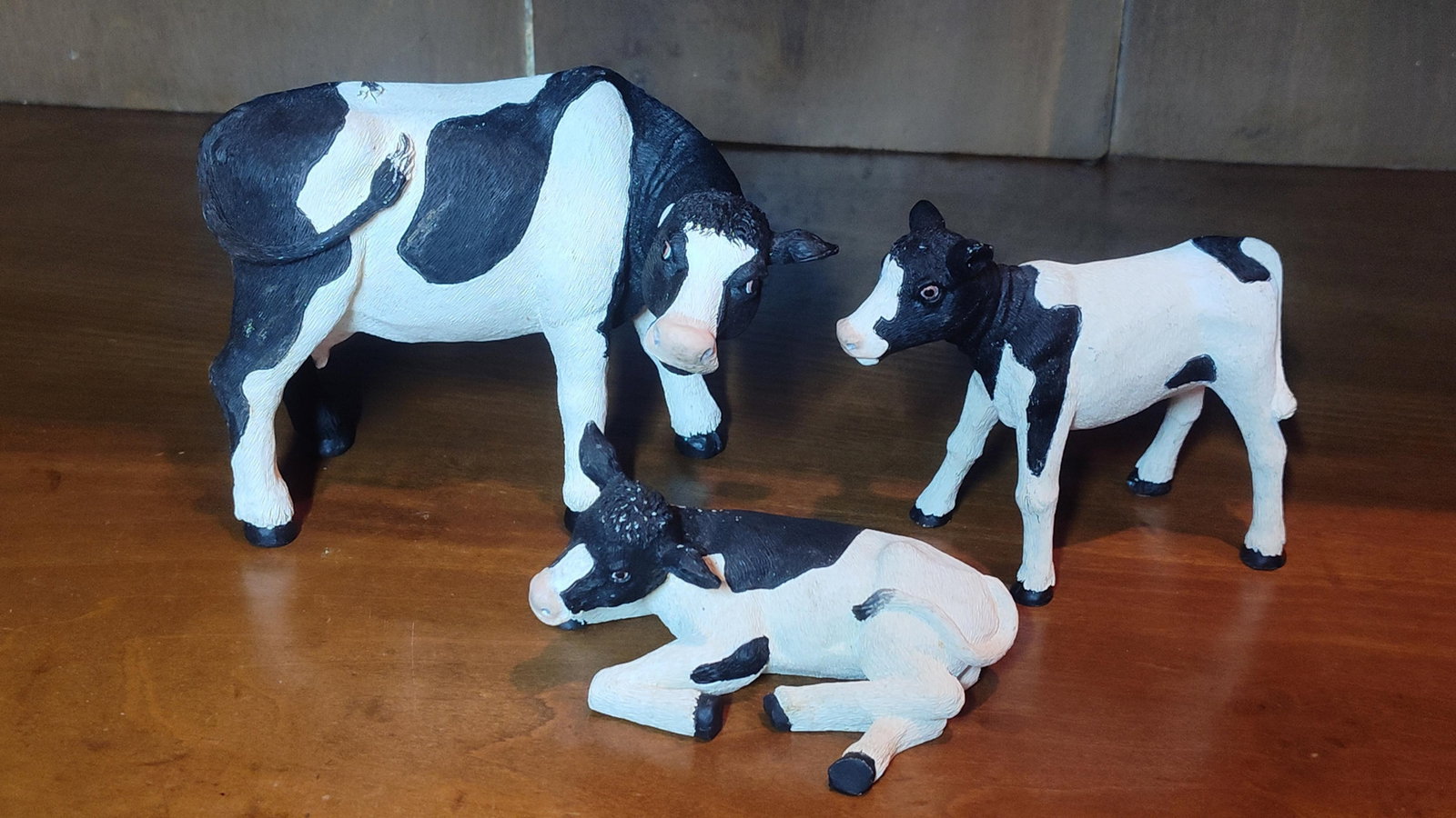 Three Holstein-Friesian Cattle Figurines: A collection of three farm animal figurines depicting a Holstein-Friesian cow, a standing calf, and a recumbent calf. These pieces are crafted from a molded composite material with a textured surface