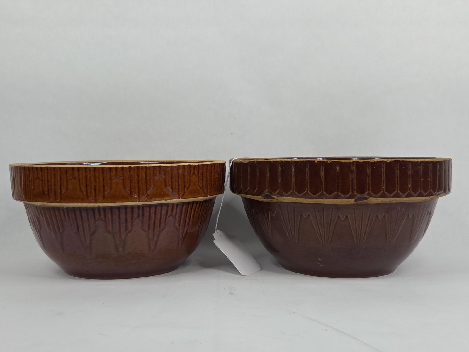 A Pair of American Brown-Glazed Picket Fence Pattern Stoneware Mixing Bowls: A pair of American brown-glazed stoneware mixing bowls in the Picket Fence pattern, frequently attributed to the Uhl Pottery Company. These circular, tapered bowls are constructed with wide, molded