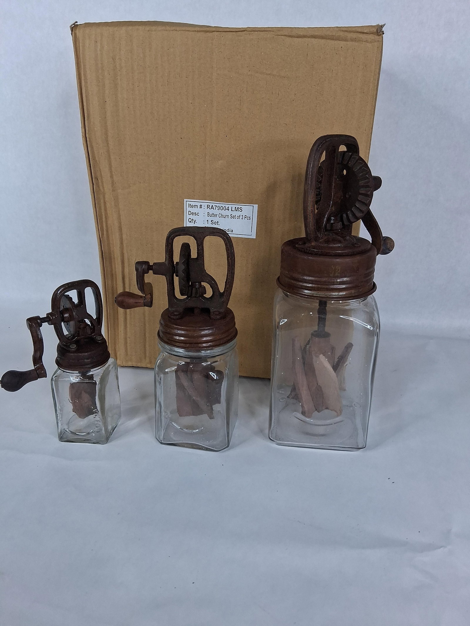 A Set of Three Decorative Graduated Glass Butter Churns in the Style of Hazel-Atlas: A set of three modern decorative hand-cranked butter churns in graduated sizes (small, medium, and large). Each churn is constructed with a rectangular clear glass jar body featuring embossed