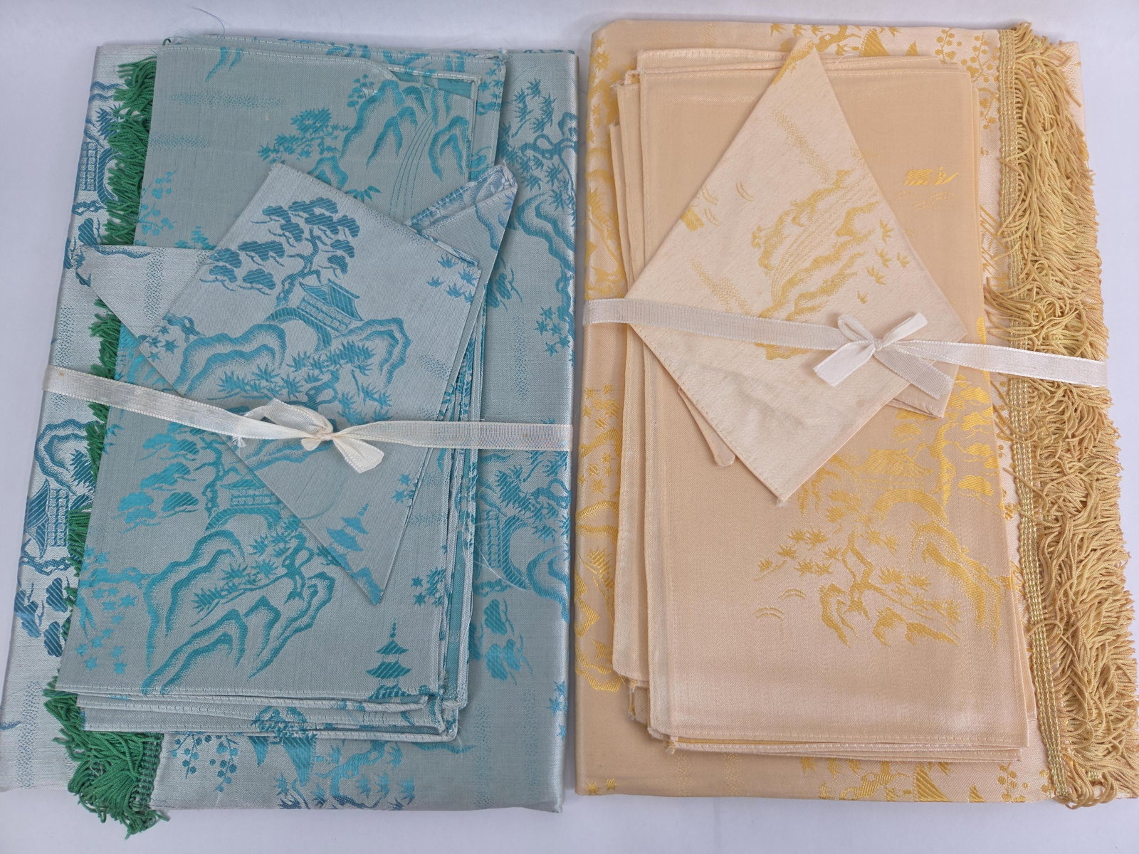 A Pair of Chinoiserie Damask Table Linen Sets: This pair of linen sets features a Chinoiserie landscape motif in a lustrous jacquard or damask weave, likely silk or high-quality rayon. Each set includes a large rectangular cloth and matching