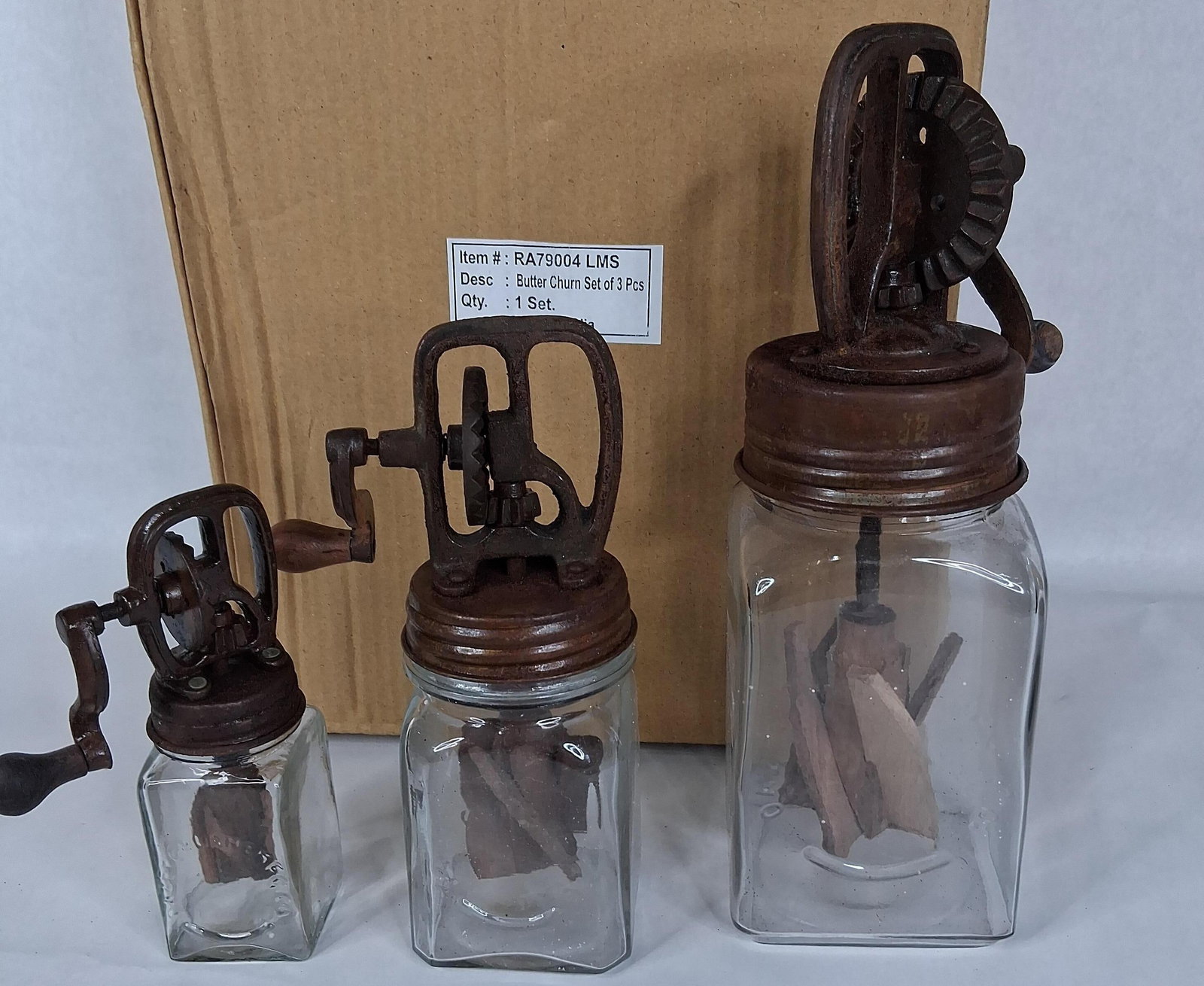 A Butter Churn Set of 3 Pcs in the Style of Dazey: This graduated set consists of three hand-crank glass butter churns. These items are contemporary decorative reproductions modeled after antique Dazey brand churns. The set includes three distinct
