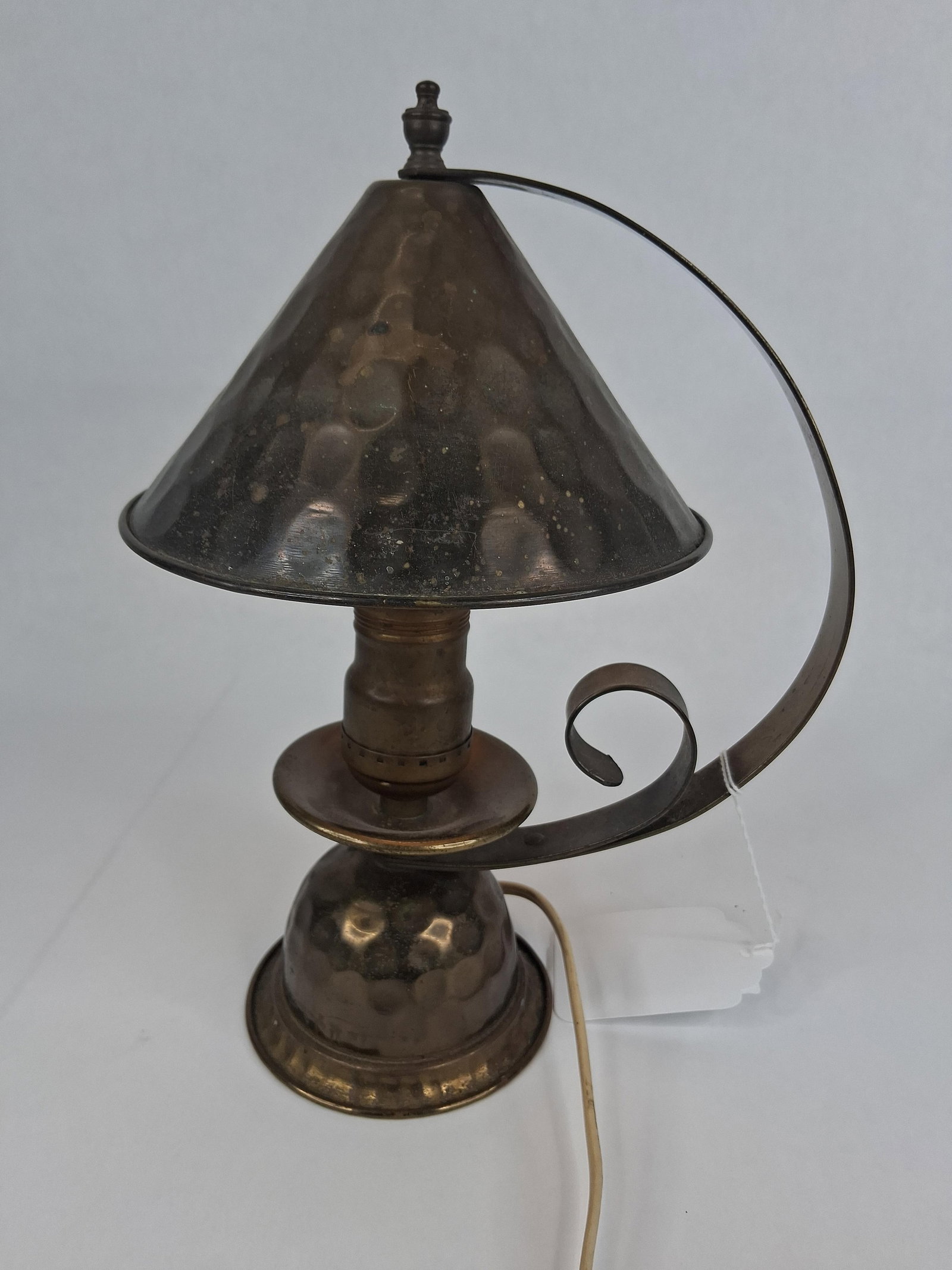 Arts and Crafts Style Hammered Copper Table Lamp: This Arts and Crafts style table lamp is constructed of hand-hammered copper featuring a dark, aged patina. The design consists of a conical metal shade supported by a single, wide-curved metal arm th