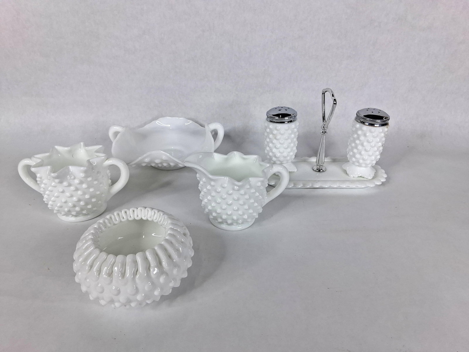 Fenton White Hobnail Milk Glass Tableware Set: This collection features an assortment of white milk glass tableware manufactured by the Fenton Art Glass Company in the hobnail pattern. The glassware is characterized by regularly spaced raised