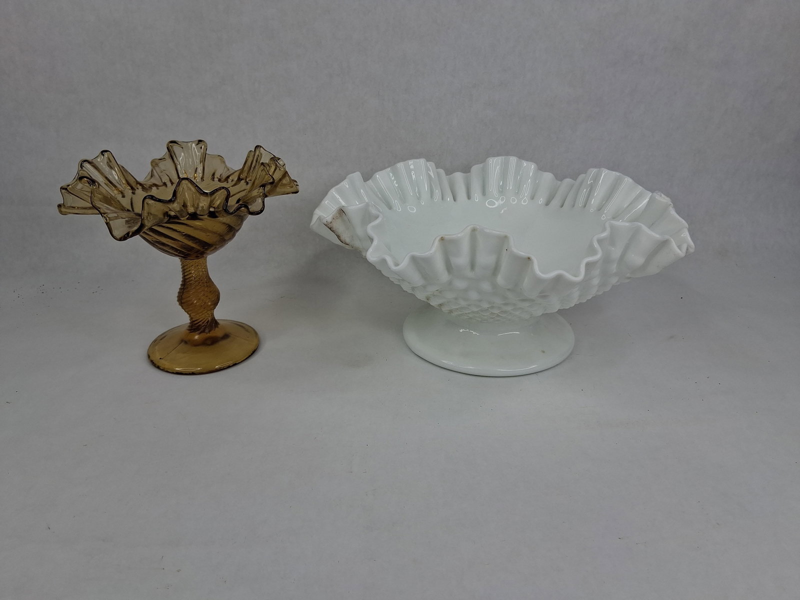 Fenton Hobnail Milk Glass Bowl & Amber Compote: This lot features two distinct examples of American decorative glass. The first is a white milk glass pedestal bowl manufactured by Fenton Art Glass. It is decorated with an exterior hobnail pattern