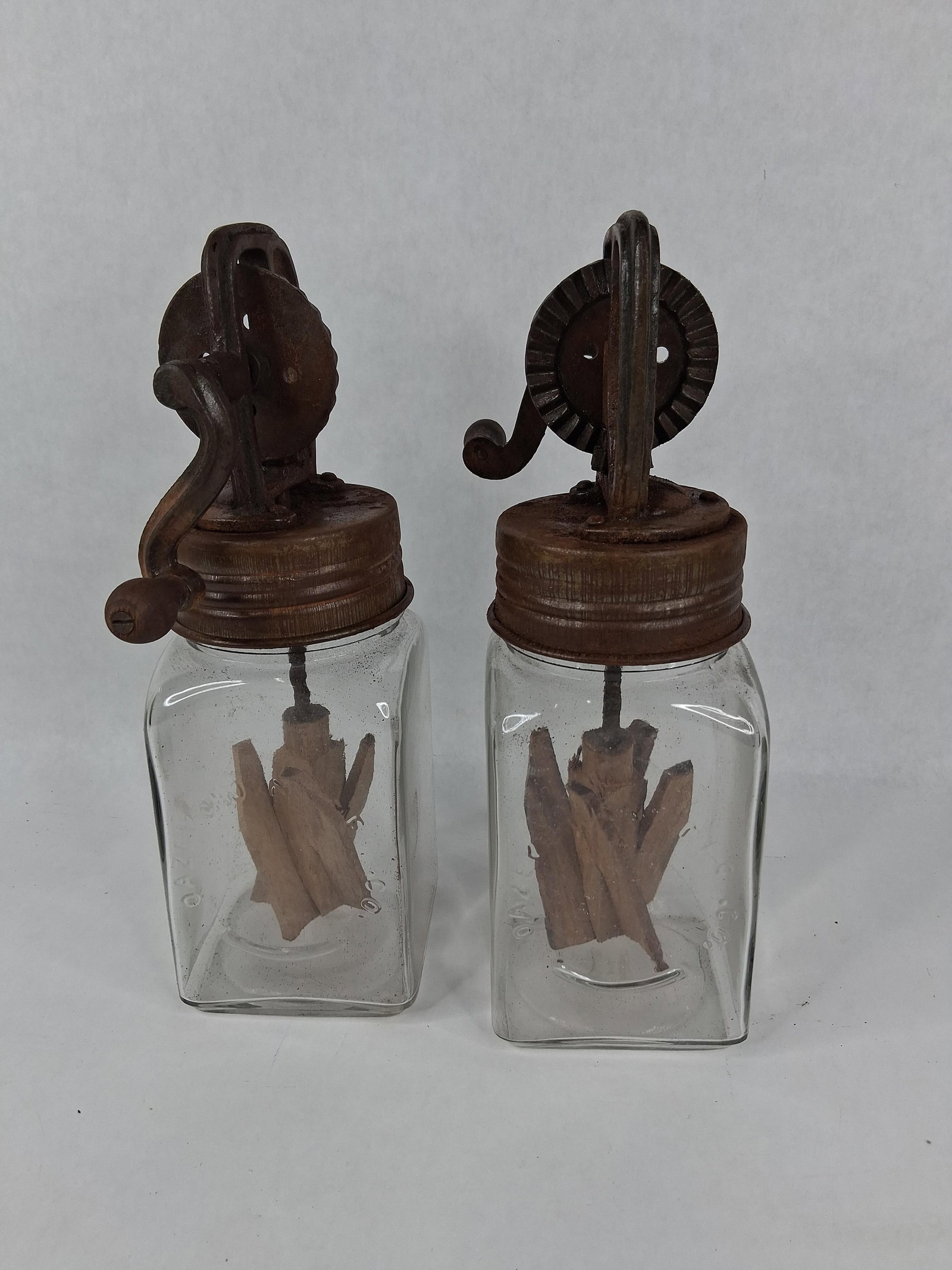 A Pair of Antique Dazey Glass Jar Butter Churns: This lot features a pair of manual hand-crank glass jar butter churns produced by the Dazey Churn and Manufacturing Company. Each churn consists of a square-sided clear glass jar with vertically