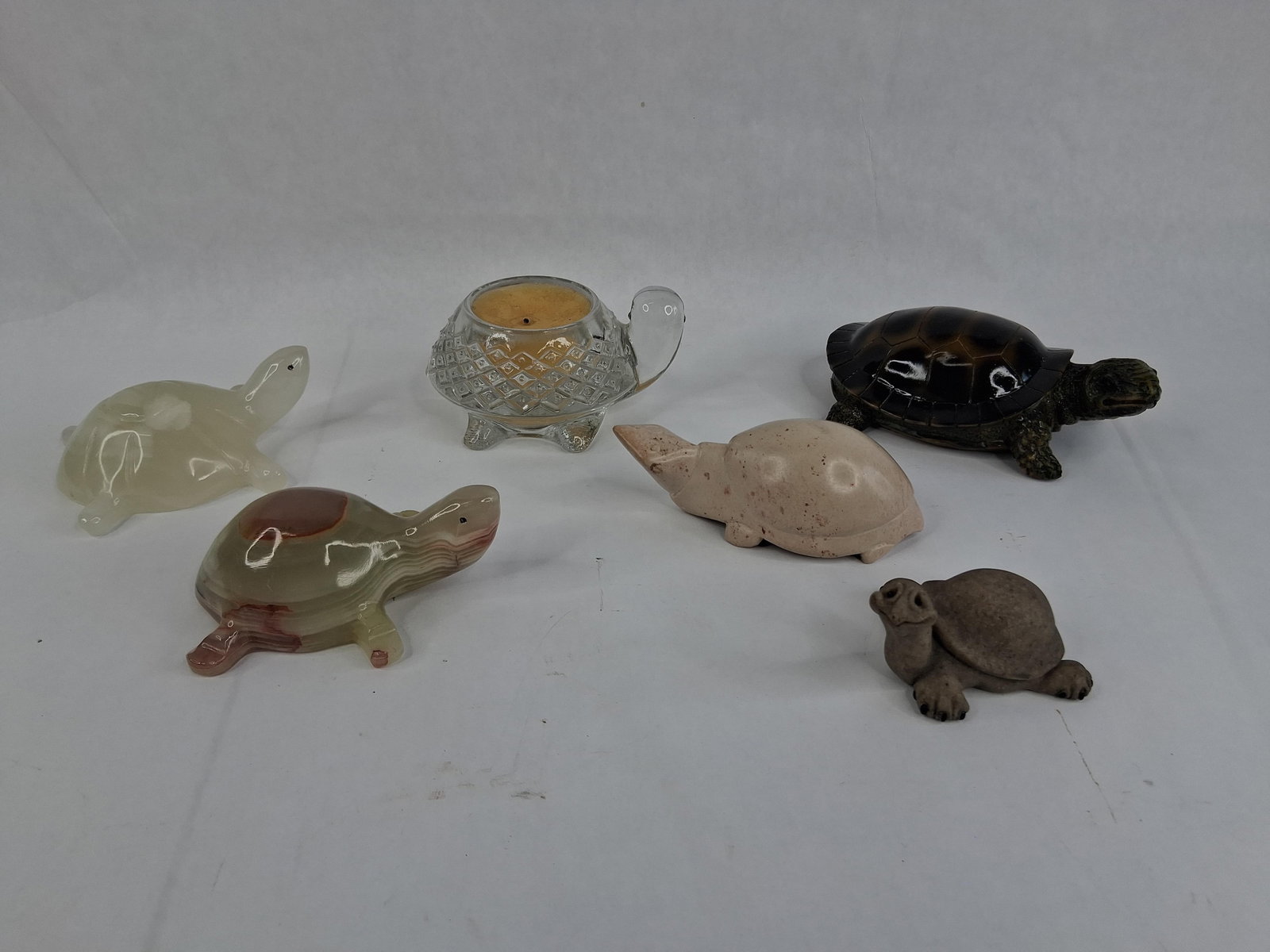 Turtle Figurines in Stone, Glass & Ceramic: This collection features an assortment of decorative turtle figurines crafted from various materials. Included are stylized turtles carved from translucent banded onyx stone. One specimen is primarily