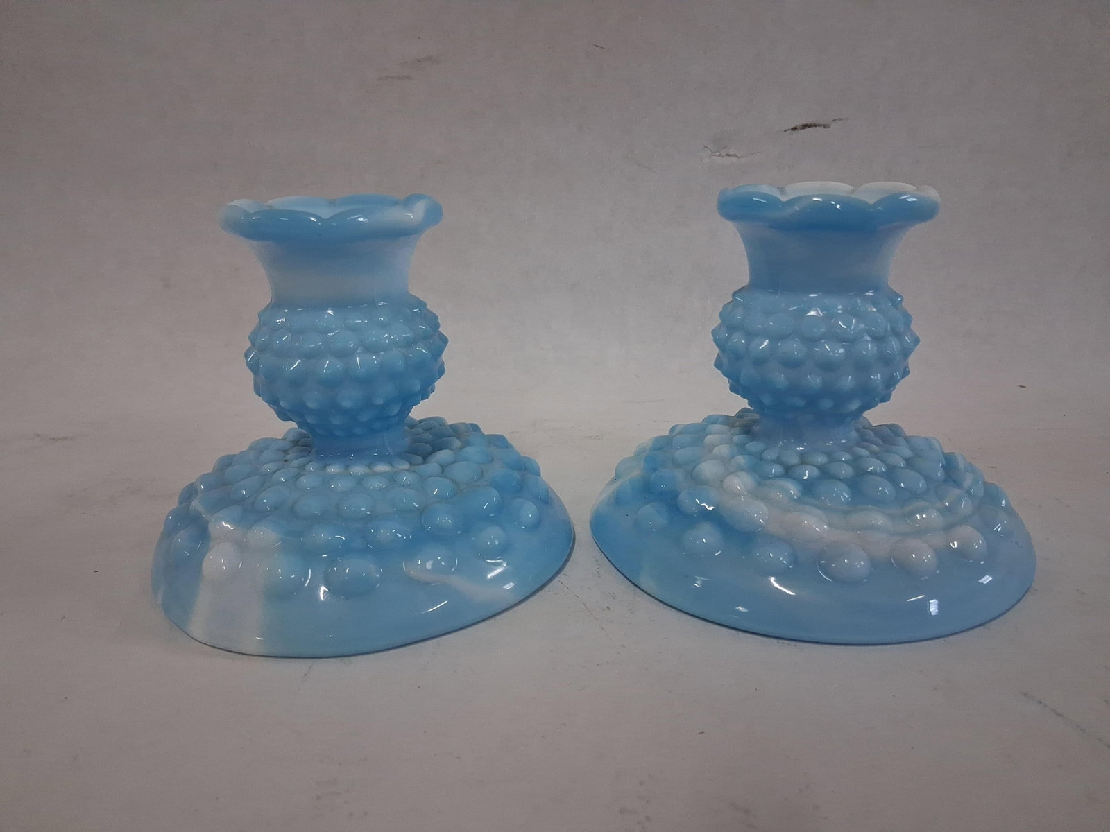 Pair Hobnail Blue Marble Slag Glass Candlesticks: A pair of candle holders crafted from blue and white marbled slag glass. Each piece features a flared circular base decorated with multiple rows of raised hobnails. The central stem is globular with