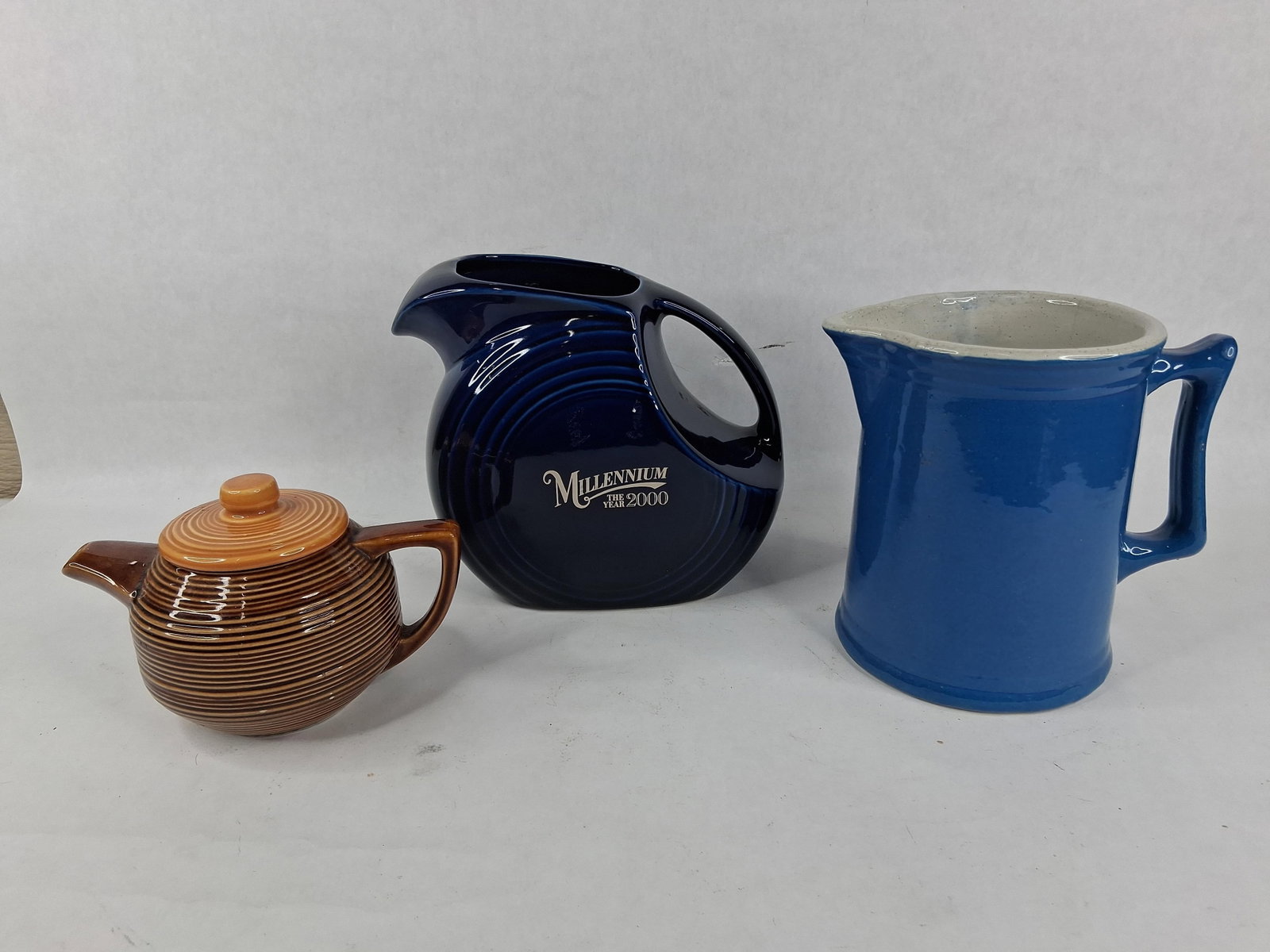 A Trio of American Ceramics Including a McCoy Teapot and a Fiesta Millennium Disc Pitcher: This collection consists of three American glazed earthenware pieces: a teapot and two pitchers. The first item is a McCoy Bermuda style ridged teapot featuring a globular form with horizontal molded