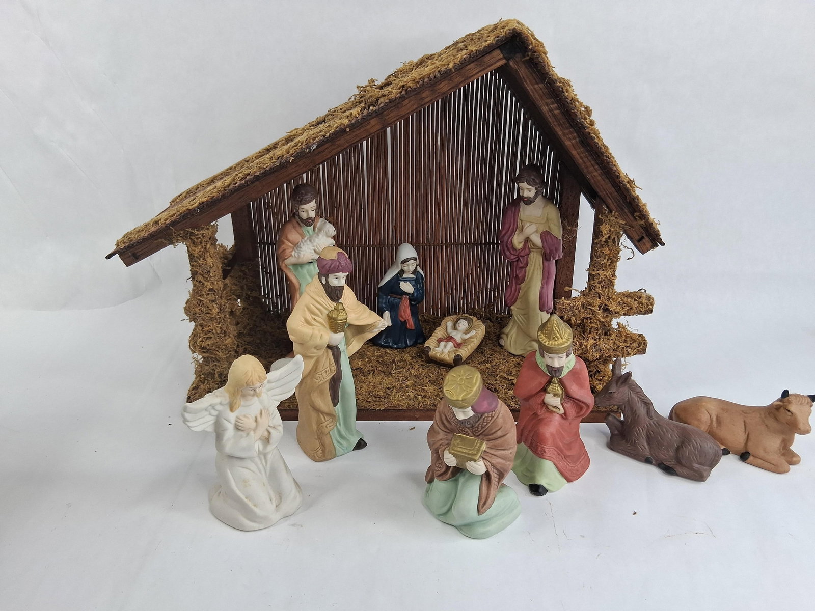 Set 11 Painted Ceramic Nativity Figurines & Stable: A nativity set comprising eleven painted ceramic figurines and a coordinating rustic stable. The figurine collection includes the Holy Family with the infant Jesus in a manger, Mary, and Joseph.