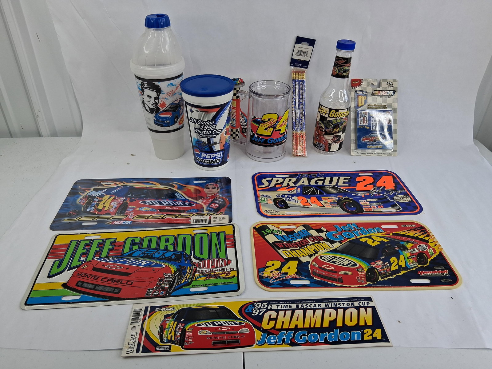 Jeff Gordon & Jack Sprague NASCAR Memorabilia: An assortment of NASCAR memorabilia primarily featuring Hendrick Motorsports driver Jeff Gordon, alongside one item representing Jack Sprague. The collection includes four decorative license plates