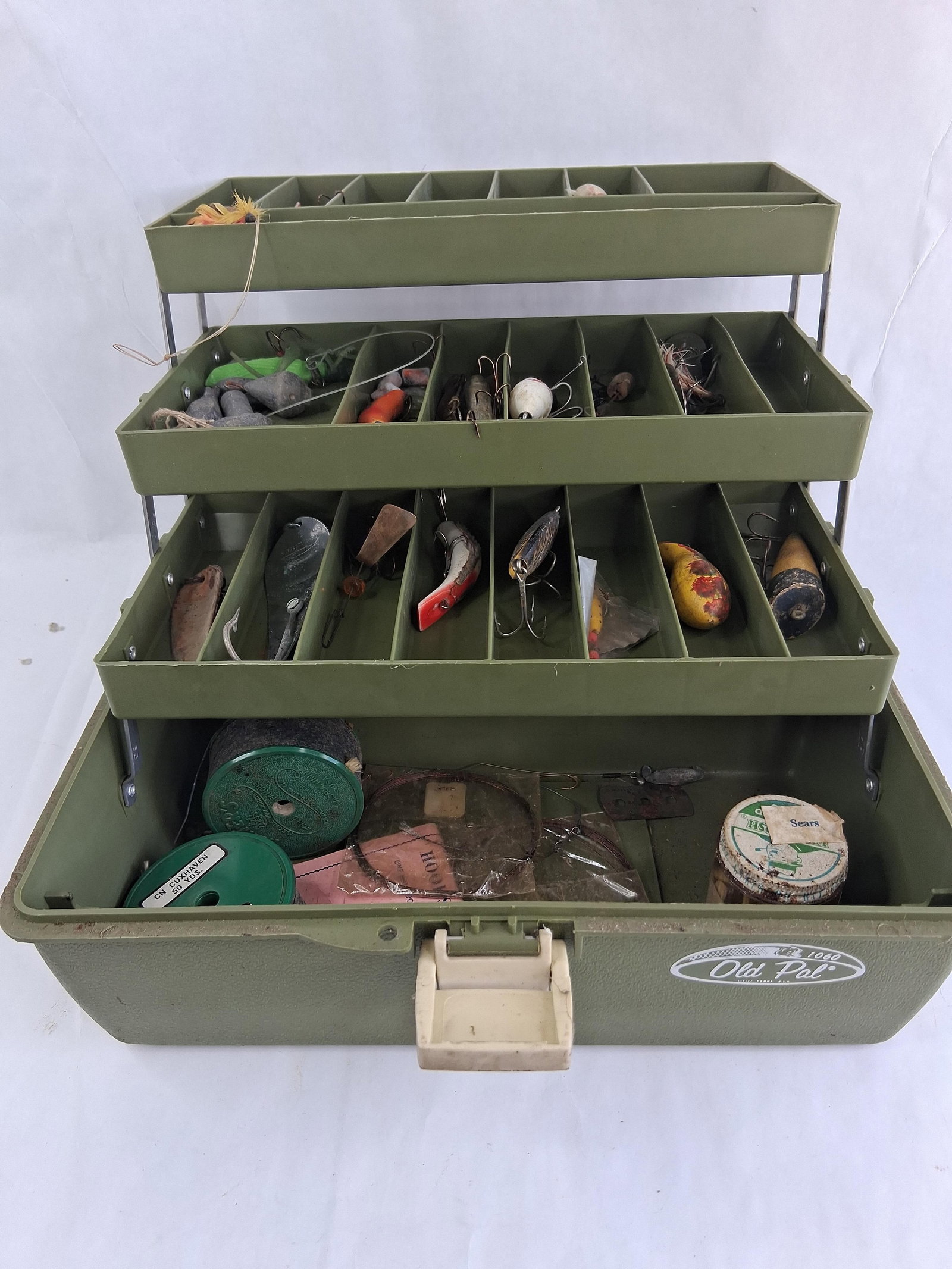 Old Pal Model 1060 Cantilevered Tackle Box with a Collection of Assorted Fishing Tackle: A Old Pal model 1060 cantilevered tackle box constructed from molded olive green plastic. The box features three tiered trays that unfold via metal brackets to reveal organized compartments, with a de