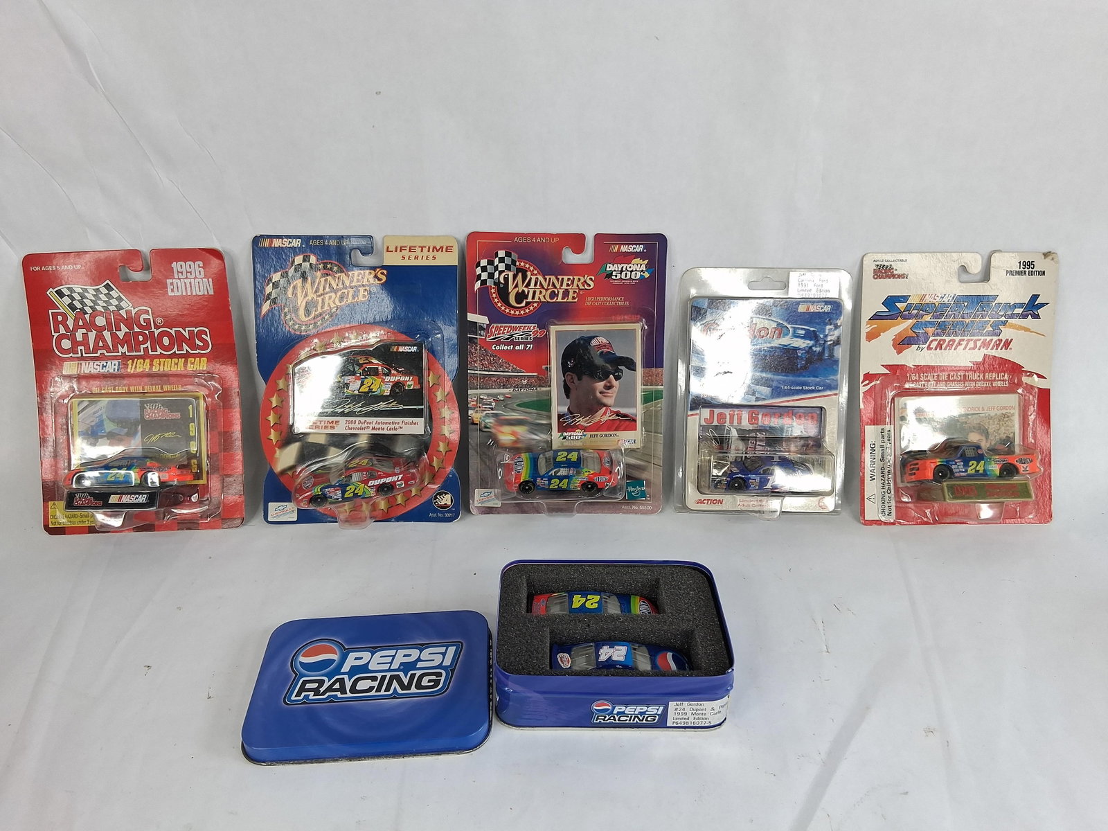 6 Jeff Gordon NASCAR 1:64 Die-Cast Sets w/ Tin: This collection features six sets of die-cast model vehicles celebrating the career of NASCAR champion Jeff Gordon. The lot includes five carded individual items and one commemorative two-car tin,