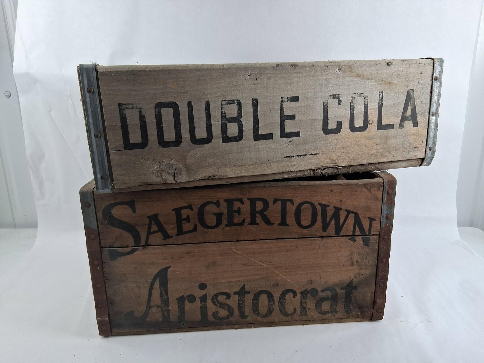 Pair PA Wooden Double Cola & Saegertown Ale Crates: This lot features two wooden beverage crates with metal reinforcements, both originating from companies in Northwestern Pennsylvania. The first item is a Double Cola crate constructed from