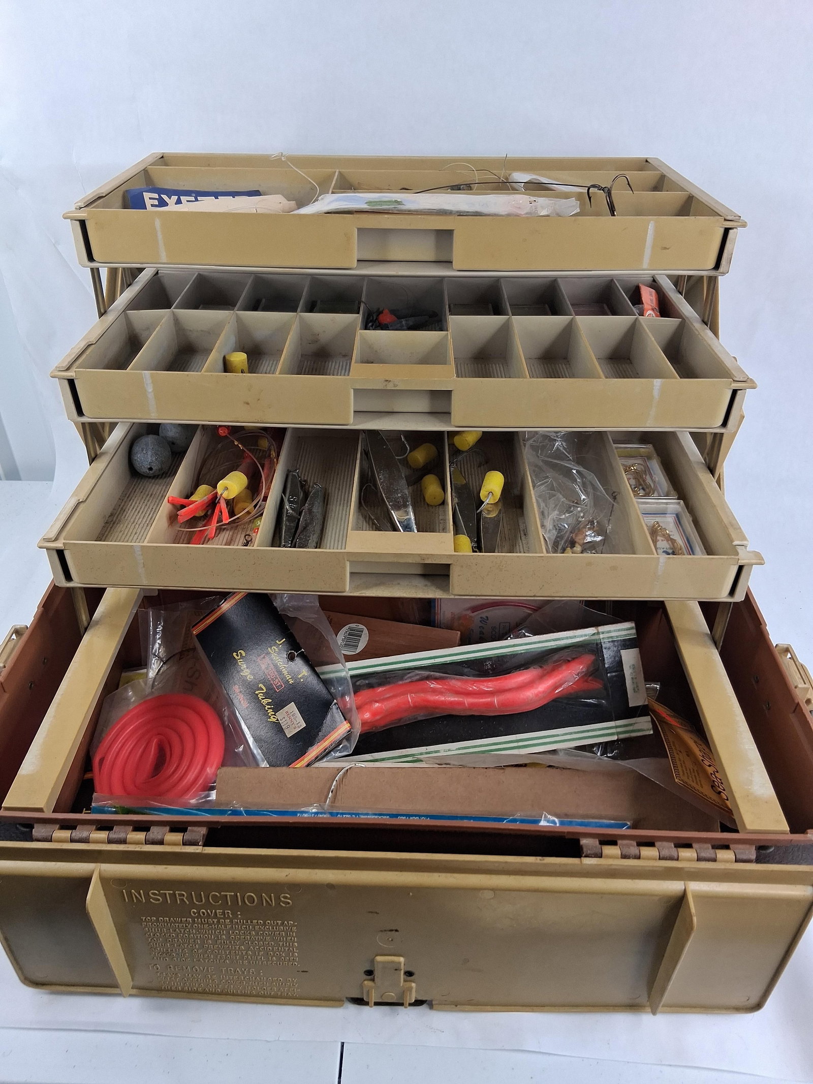 Plano 727 Cantilever Tackle Box w/ Tackle: A Plano 727 plastic cantilever tackle box featuring a tan lid and brown base. The model number 727 is embossed on the front of the lid and the latch mechanism displays the Plano logo. The interior