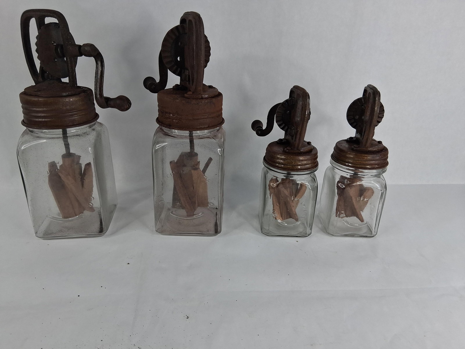 Four Dazey Antique Glass and Cast Iron Hand Crank Butter Churns: This lot consists of four hand-crank butter churns produced by the Dazey Churn & Mfg. Co. of St. Louis, Missouri. The collection includes two larger units and two smaller units. Each churn is composed