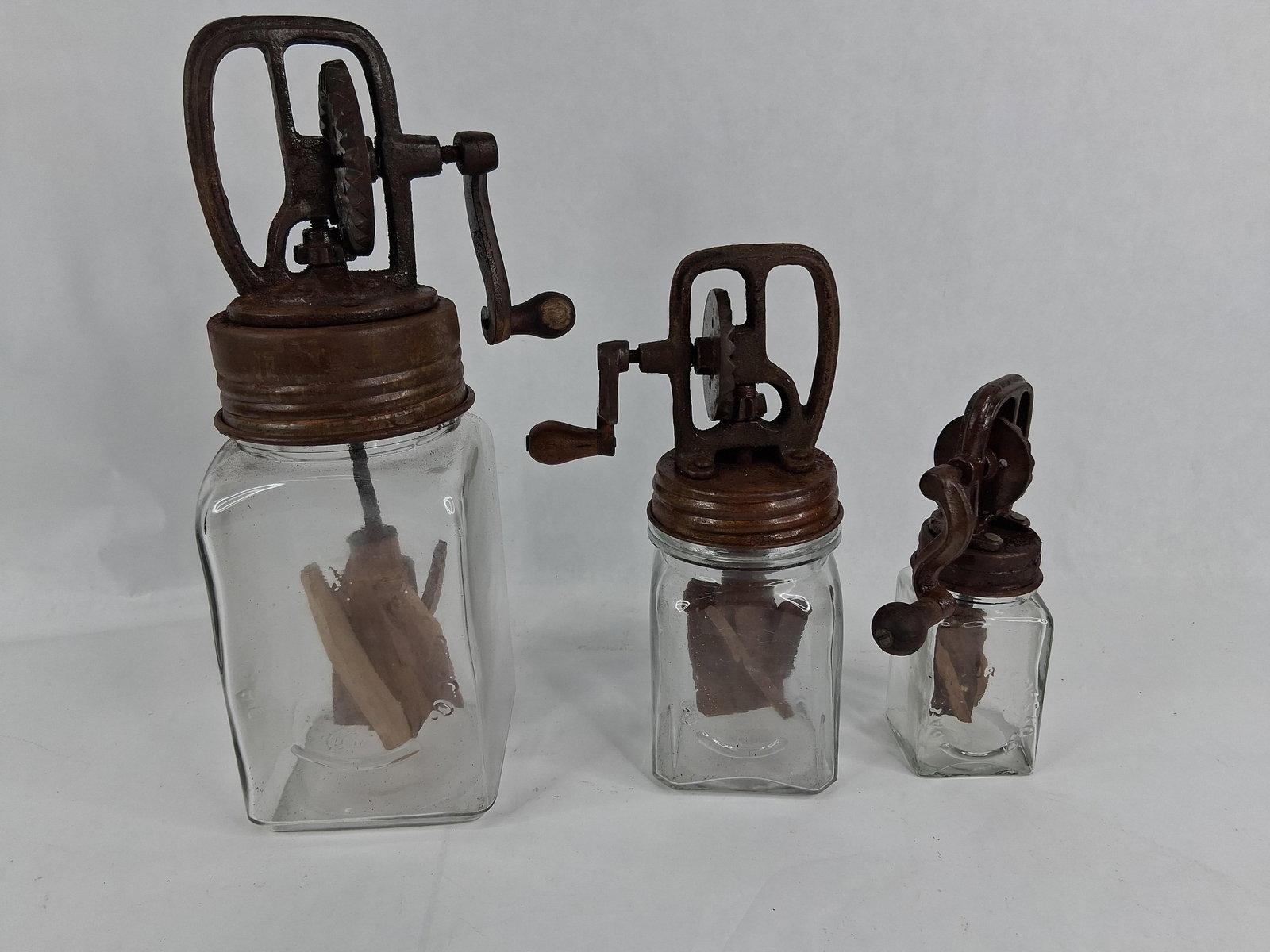 A Trio of Antique Dazey Glass Jar Butter Churns: A trio of antique hand-cranked glass jar butter churns in graduated sizes, identified by the markings and construction as products of the Dazey Churn and Manufacturing Company. Each churn consists of 
