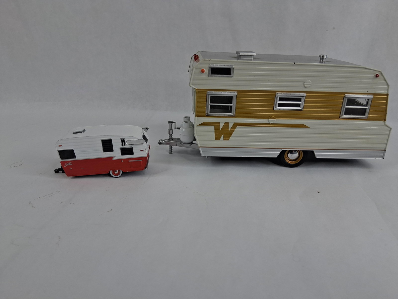 Pair GreenLight Winnebago & Shasta Travel Trailers: This lot comprises a pair of 1:24 scale model travel trailers. Both items are constructed from die-cast metal with plastic components. The first model is a replica of a 1964 Winnebago 216