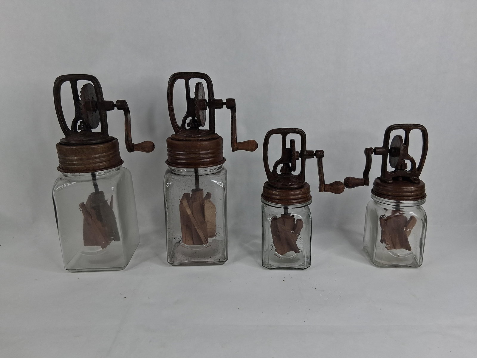 Group Daisy Brand Hand-Crank Glass Butter Churns: largest is 11.5 in smallest is 8.5 This group includes multiple antique hand-cranked butter churns in two distinct sizes. Each unit consists of a clear glass jar with a square profile and a screw-top 
