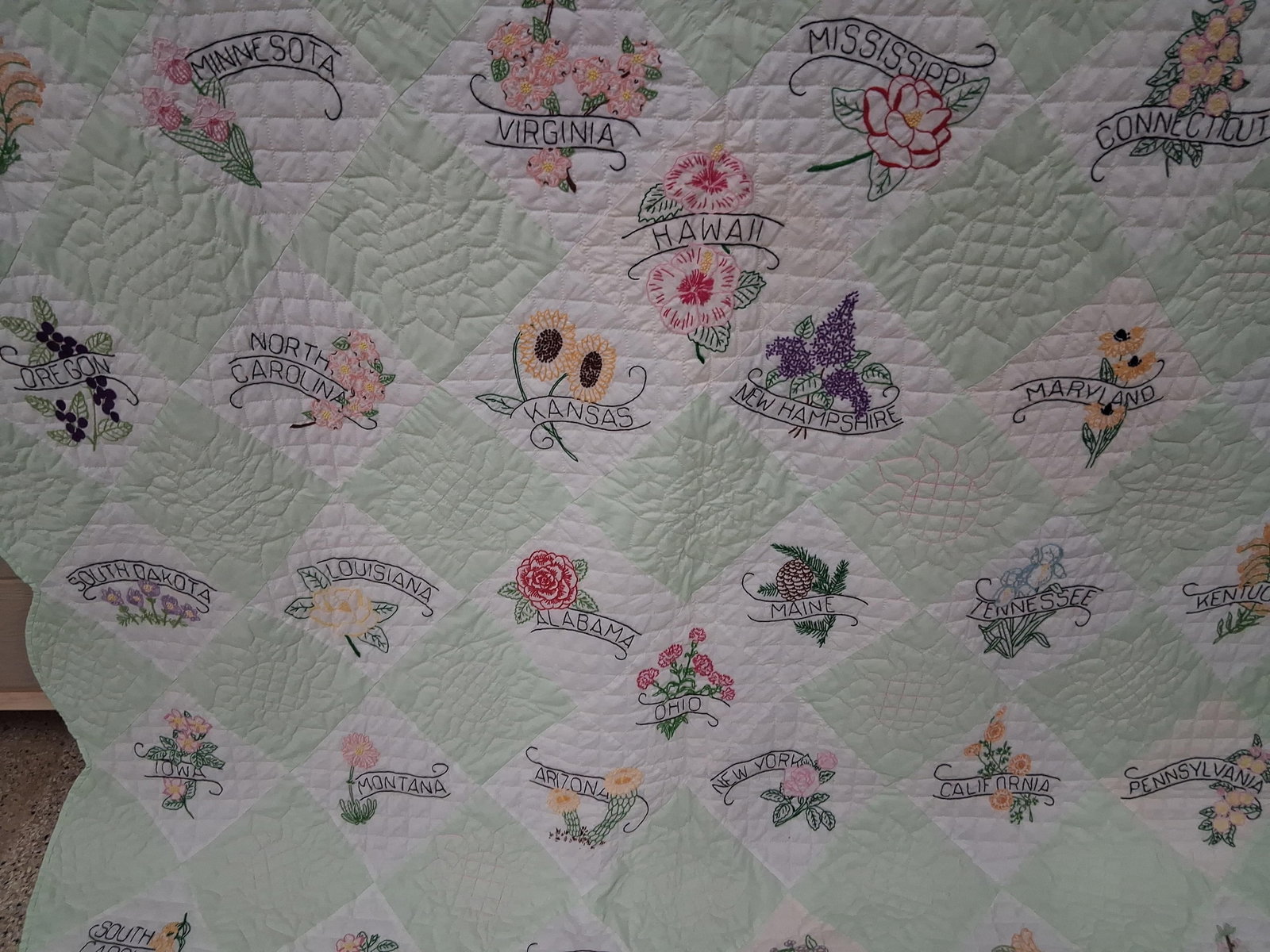 Mid-20th C. Embroidered 50 US State Flower Quilt: 70x95This mid-twentieth century quilt features a complete series of hand-embroidered floral motifs representing the 50 U.S. states. The design follows a diagonal checkerboard pattern, alternating