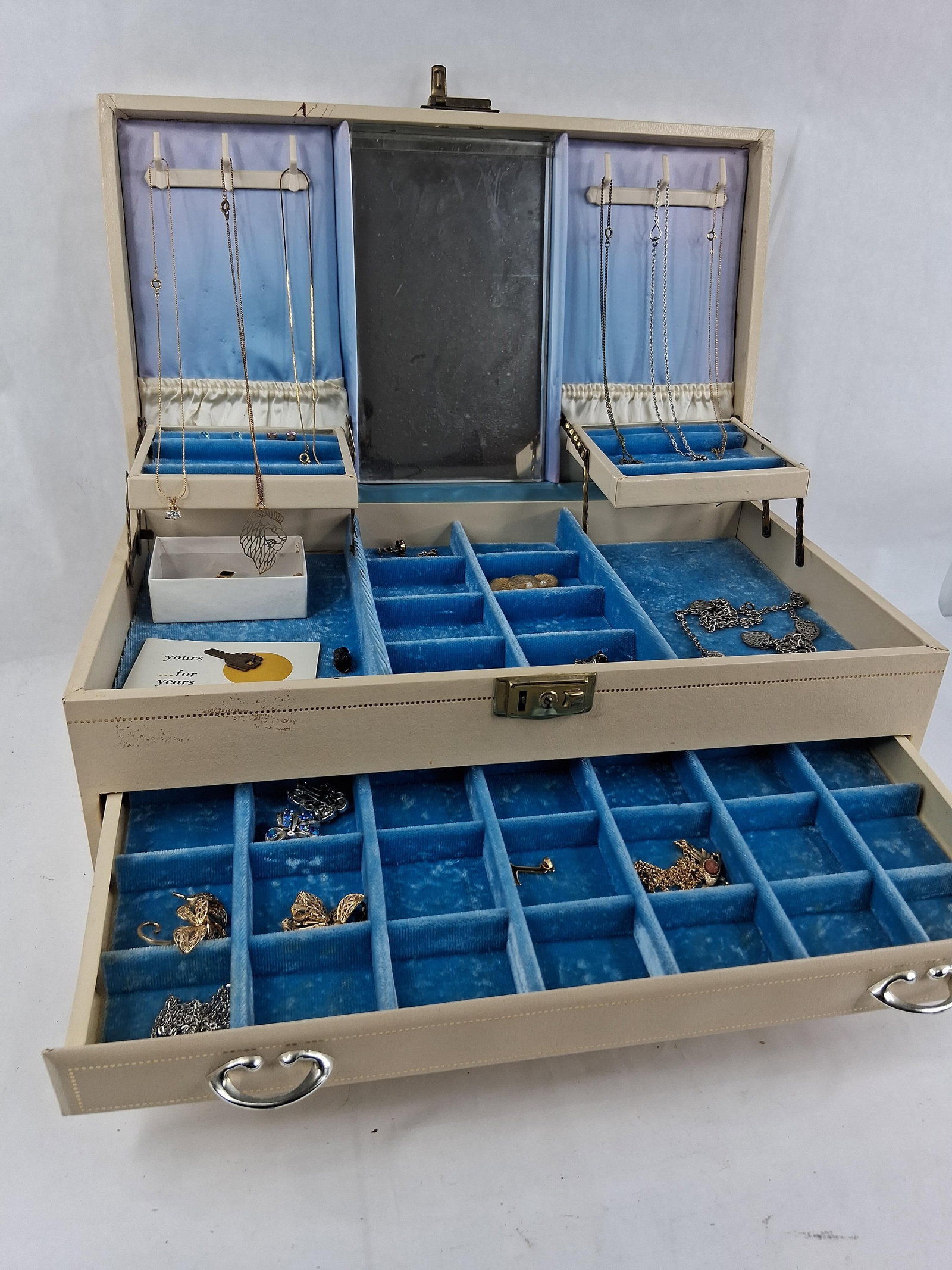 Faux Leather Jewelry Box w/ Costume Jewelry: This collection features a three-tier jewelry box, attributed to Mele, containing an assortment of mid-to-late 20th-century costume jewelry. The rectangular box is finished in a beige textured vinyl o