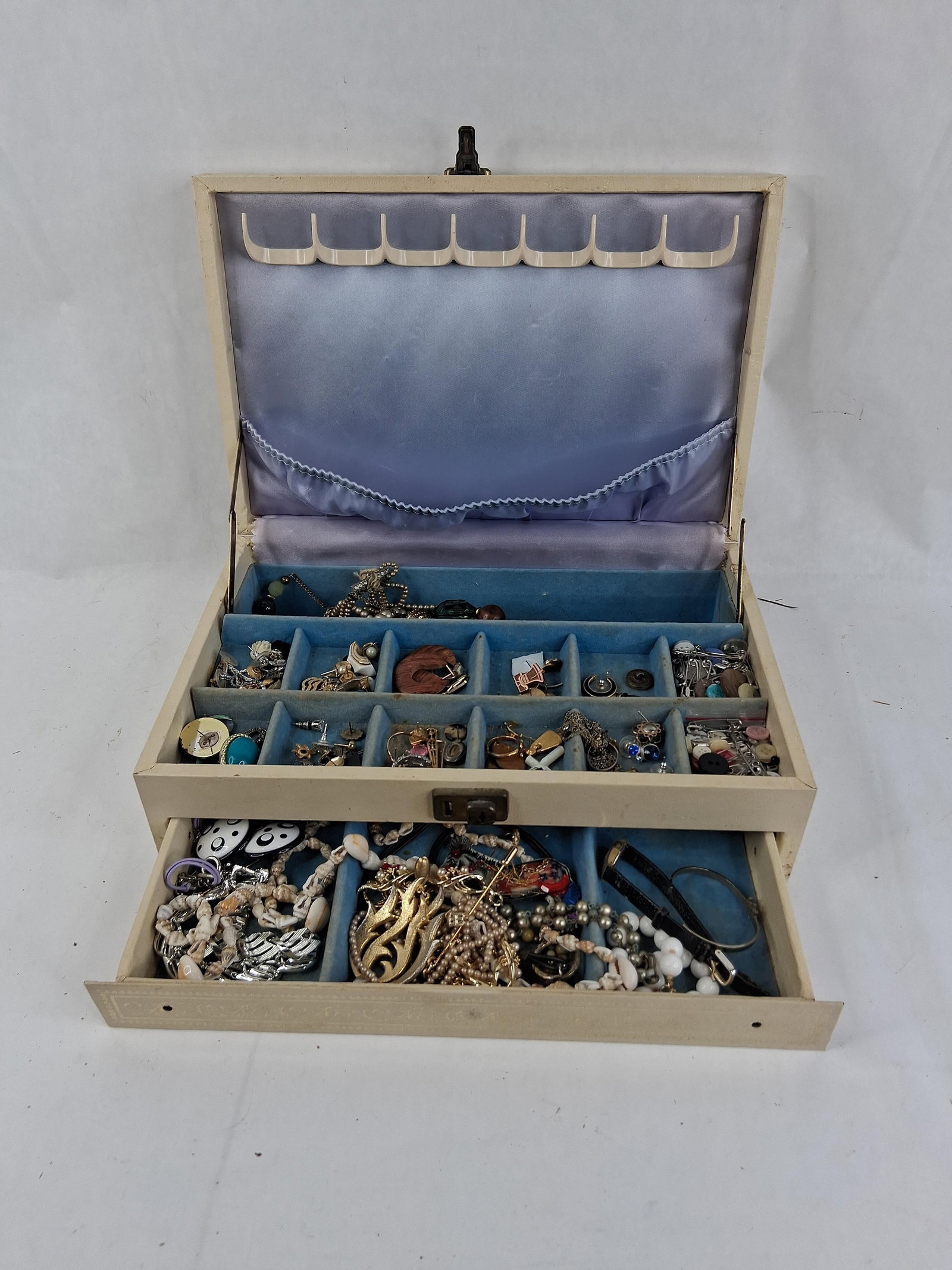 Two-Tier Jewelry Box with an Assortment of Costume Jewelry, Watches, and Buttons: This lot features a two-tier jewelry box containing an extensive collection of mid-to-late 20th-century costume jewelry and accessories. The jewelry box is constructed with a cream-colored vinyl exter