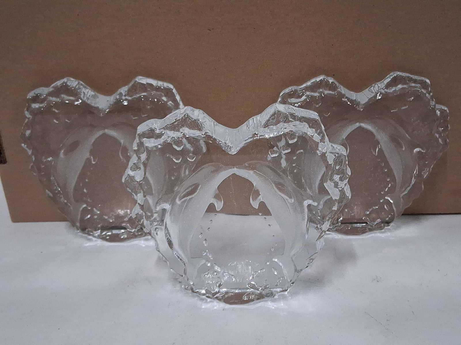 Trio Textured Glass Dolphin Votive Candle Holders: A trio of molded glass votive candle holders. Each piece features a maritime motif with two dolphins leaping toward one another, their noses meeting at the center. The dolphin figures are executed