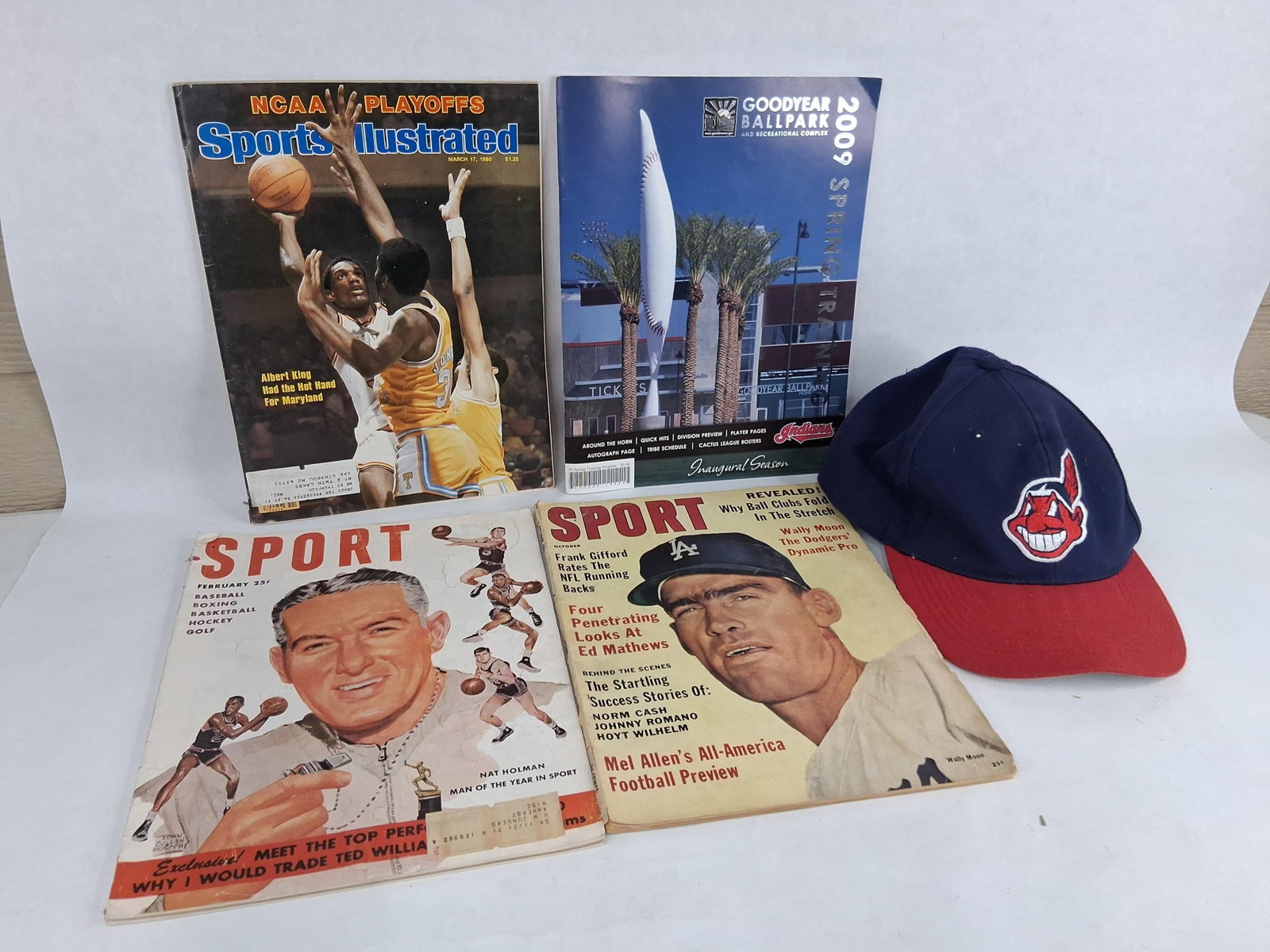 Sports Magazines, Spring Program & Indians Cap: An assortment of sports memorabilia consisting of periodicals and apparel. The collection includes a February 1951 issue of SPORT magazine featuring an illustration of Nat Holman as Man of the Year