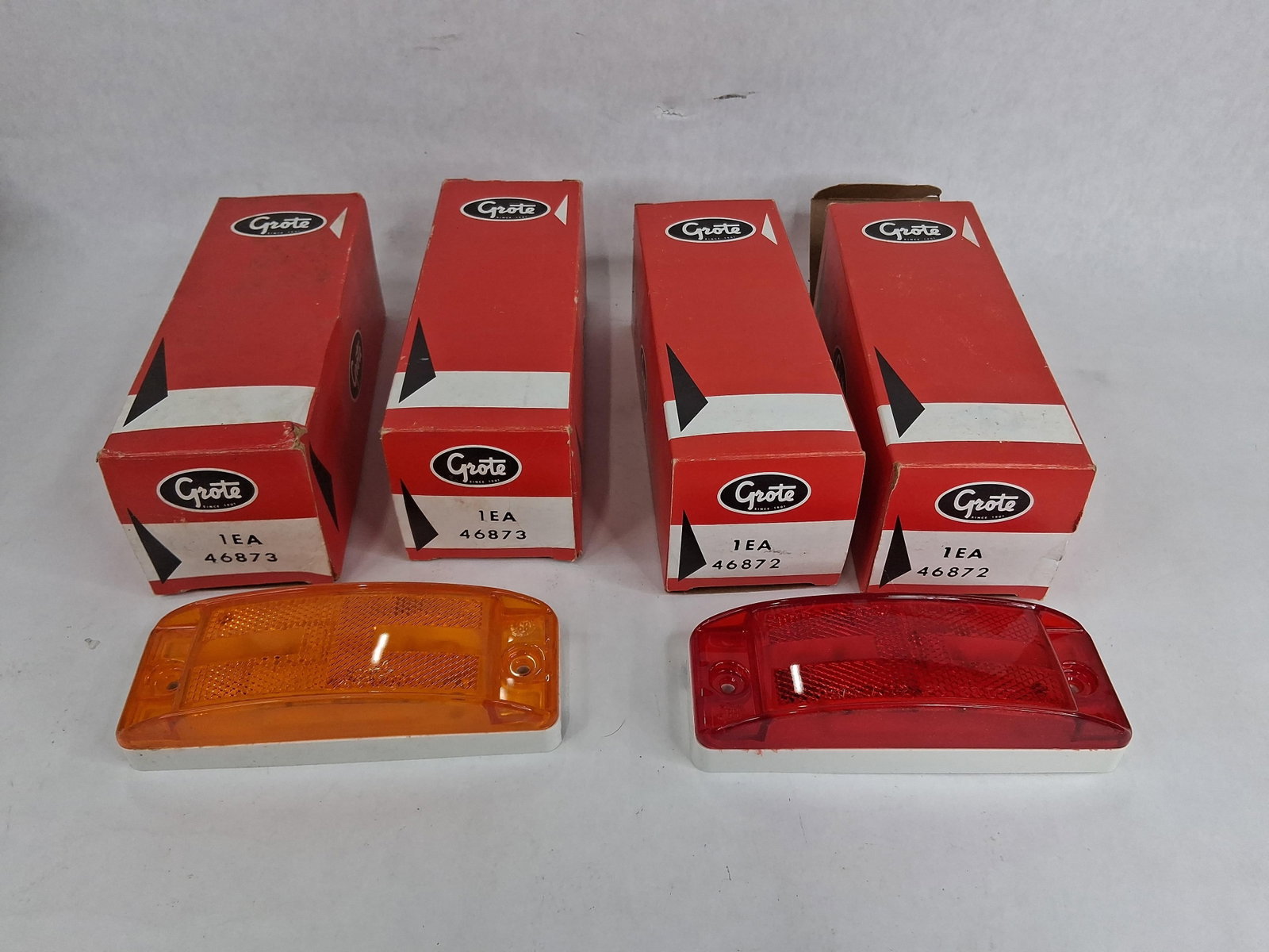 A Group of Four Grote New Old Stock Turtleback II Clearance and Marker Lights with Original Boxes: A collection of four automotive clearance and side marker lamps manufactured by Grote. The group consists of two amber lamps, model number 46873, and two red lamps, model number 46872, all