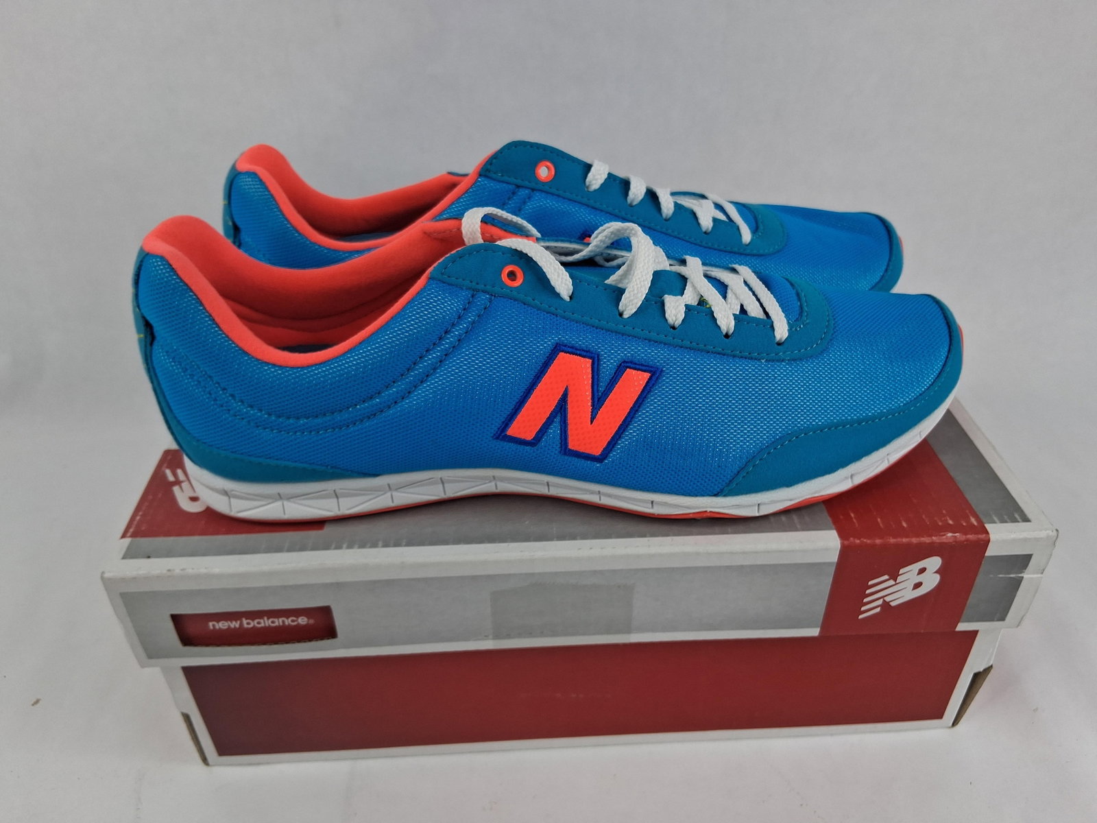 Pair New Balance WL792BC Running Course Sneakers: A pair of New Balance WL792BC Running Course low-profile athletic shoes. The uppers are constructed from a bright blue synthetic mesh with tonal synthetic overlays. The design features neon orange acc