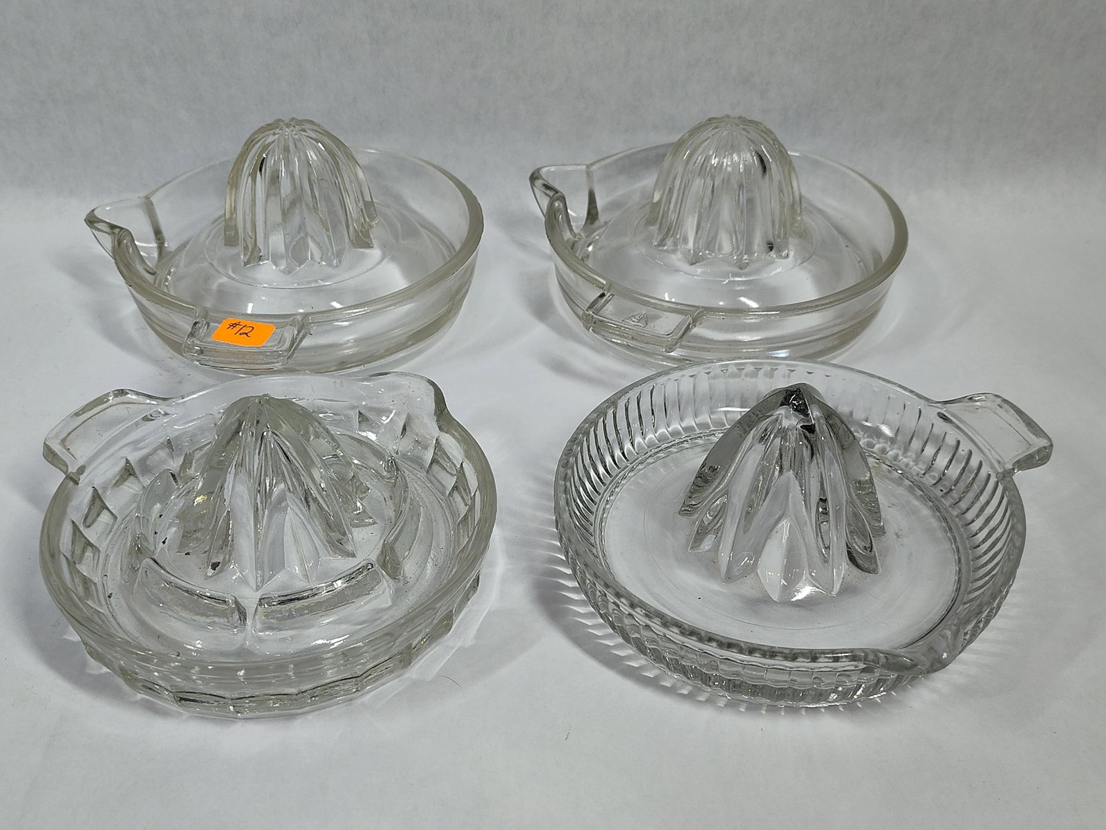 Hazel-Atlas Set 4 Pressed Glass Citrus Reamers: This lot consists of four vintage clear pressed glass citrus reamers featuring three distinct styles of construction. One juicer is embossed on the handle with the Hazel-Atlas Glass Company mark,