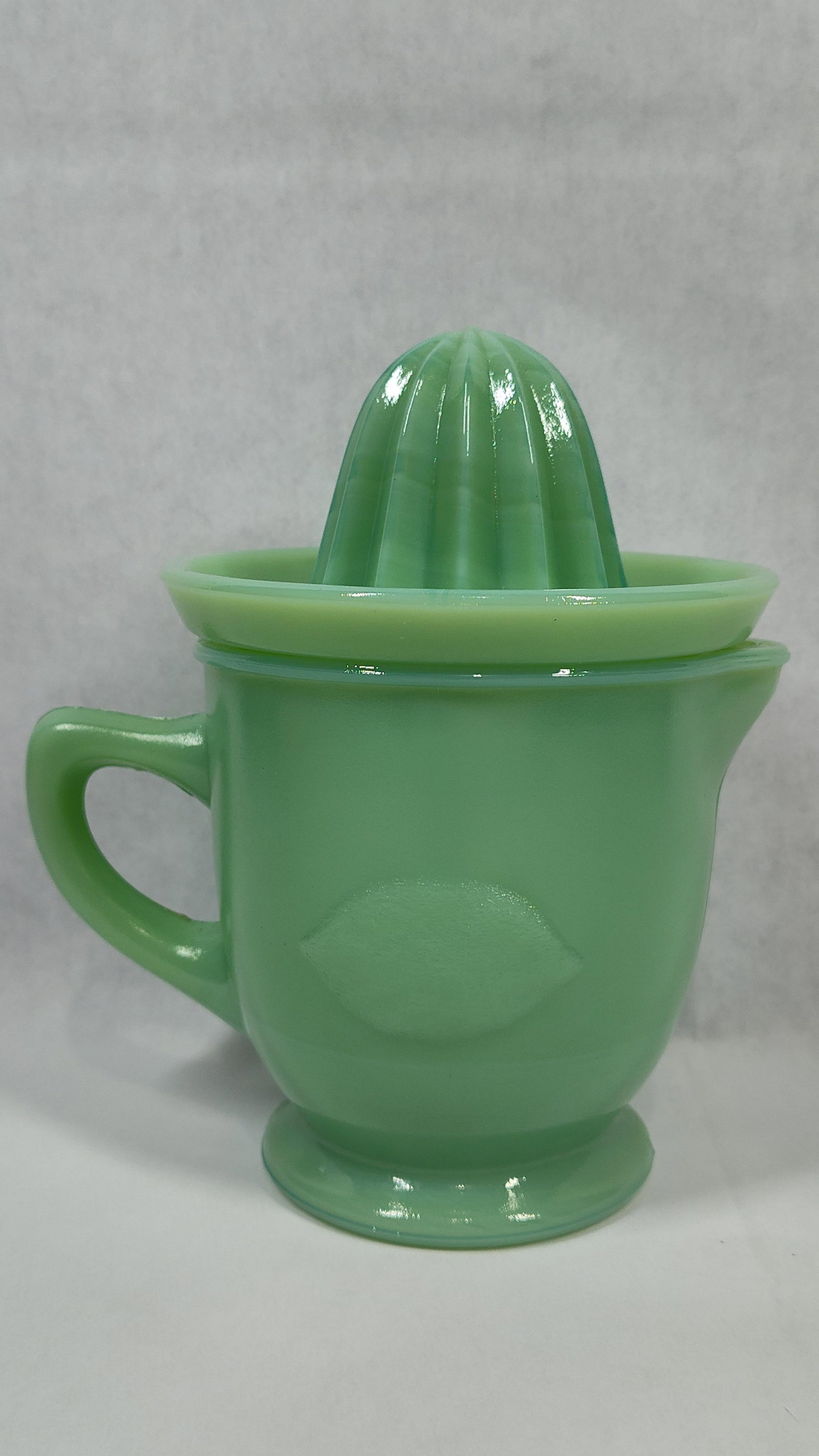 Vtg Jadeite Glass Citrus Juicer & Pitcher Set: This vintage two-piece citrus juicer set is attributed to the Jeannette Glass Company. It is crafted from opaque mint green pressed glass, a material commonly known as Jadeite or Jadite. The set consi