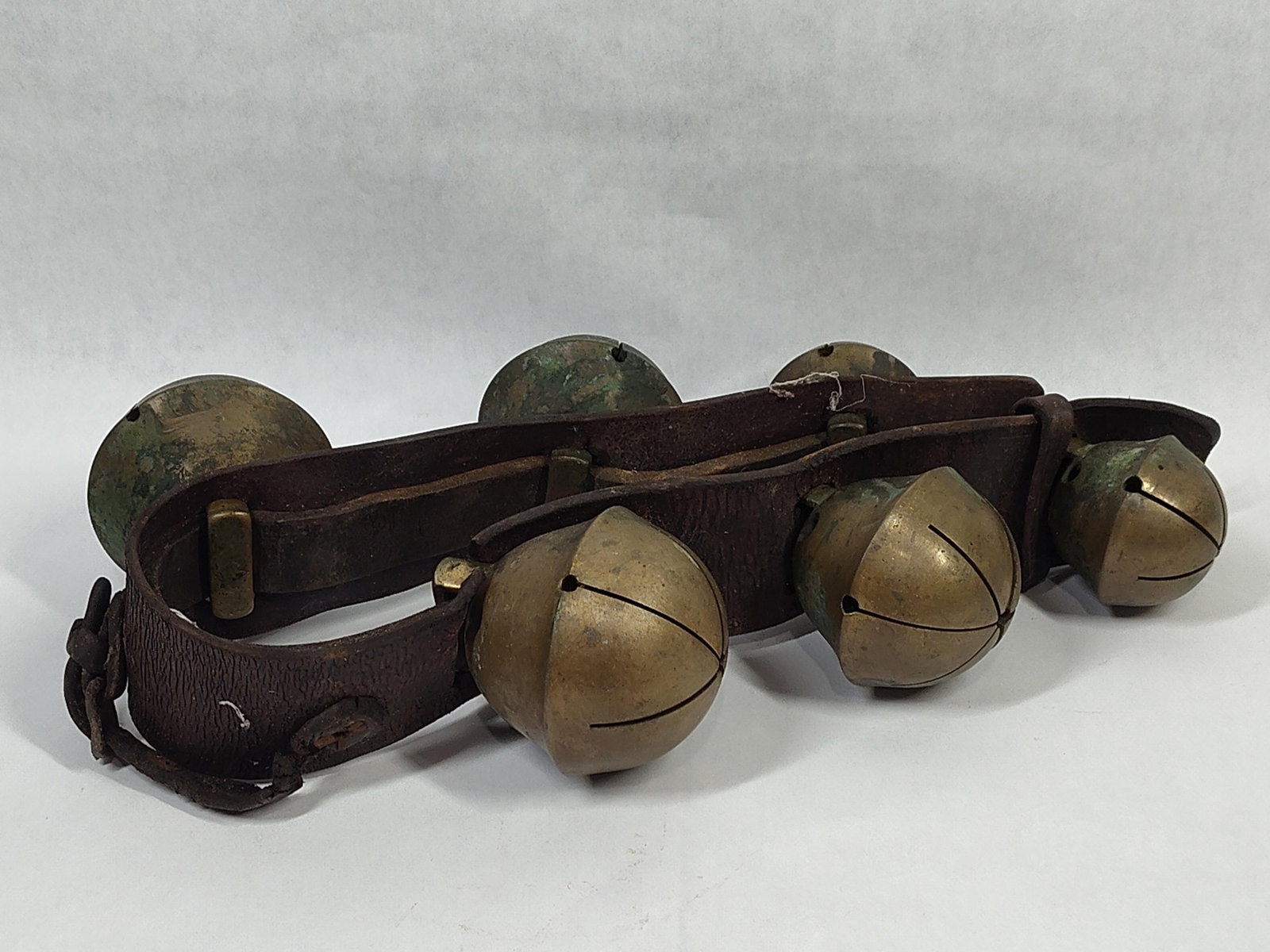 A Pair of Leather Straps with Cast Brass Crotal Sleigh Bells: This lot features a pair of matching leather straps, each mounted with three large cast brass or bronze crotal bells. The bells are spherical in form with a traditional cross-cut petal opening on the