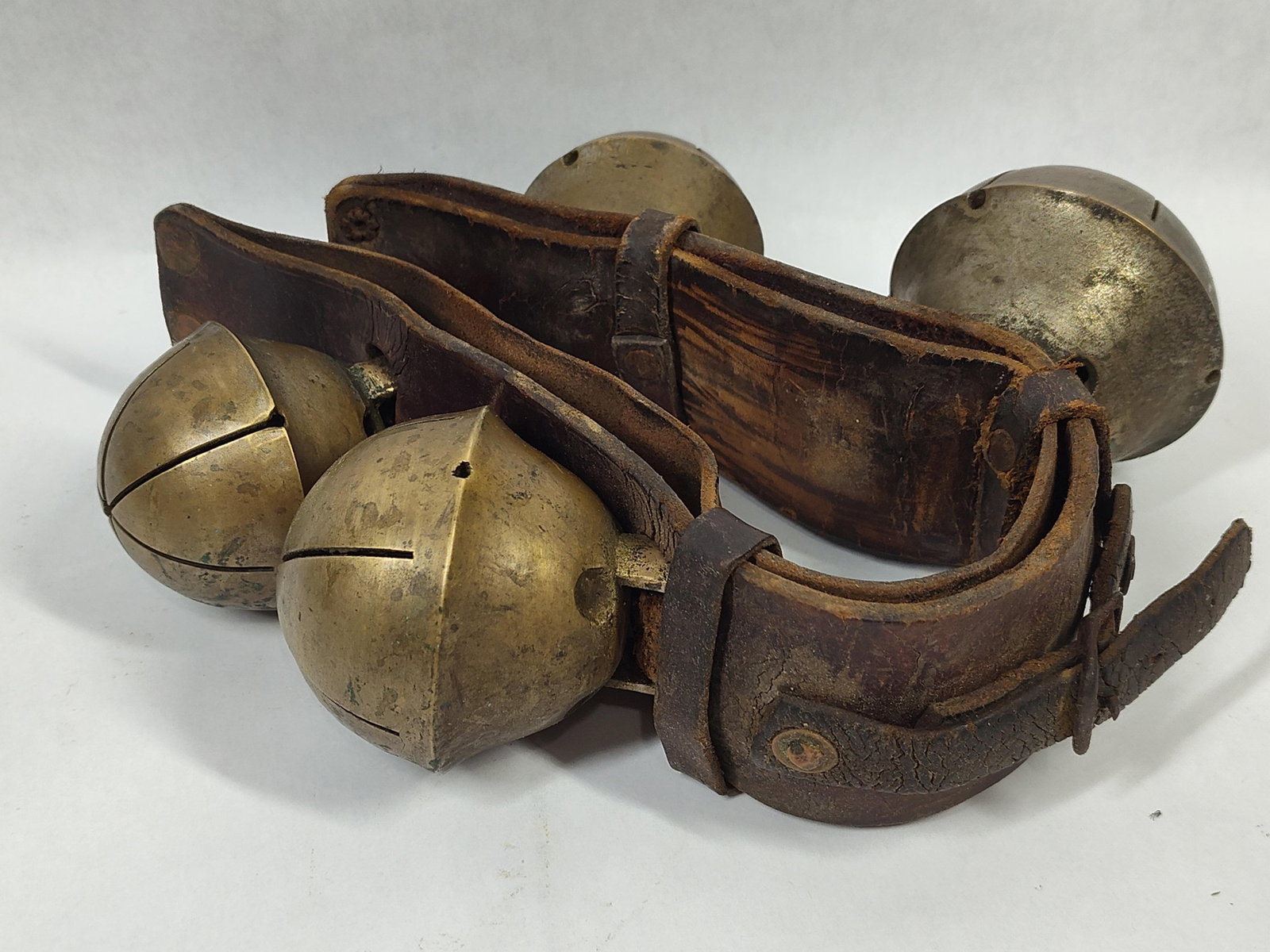 A Set of Antique Brass Swedish Style Rump Strap Sleigh Bells on Leather: A set of antique crotal-style sleigh bells mounted on a heavy, double-layered dark brown leather strap. This configuration is characteristic of a horse rump strap used in the Swedish or Swiss