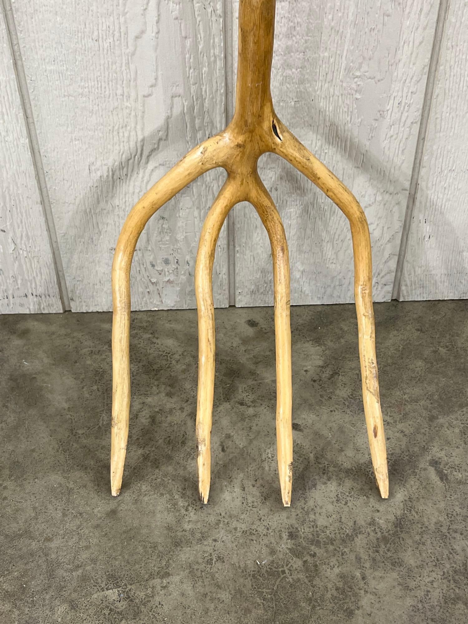 Hand-Carved Single-Branch 4-Tine Wood Pitchfork: This primitive agricultural implement is a hand-carved four-tine wooden pitchfork, crafted from a single branched limb. The tool features a long, tapered handle that transitions into four integral,