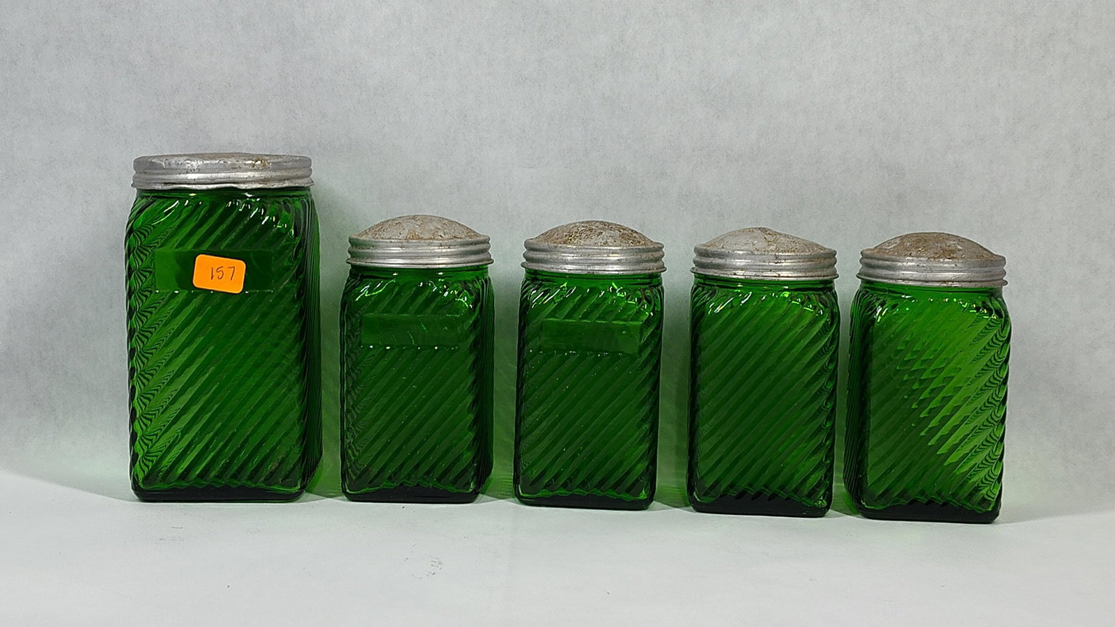 Owens-Illinois Green Hoosier Canisters & Shakers: This set of vintage kitchen glassware was manufactured by the Owens-Illinois Glass Company. The items are crafted from transparent emerald green glass and feature a square footprint with a diagonal